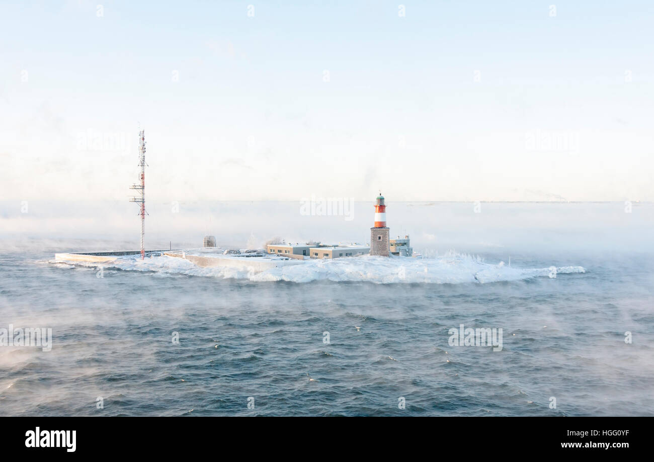 Lighthouse and telecommunication antenna on an isle in a vaporing sea at winter Stock Photo