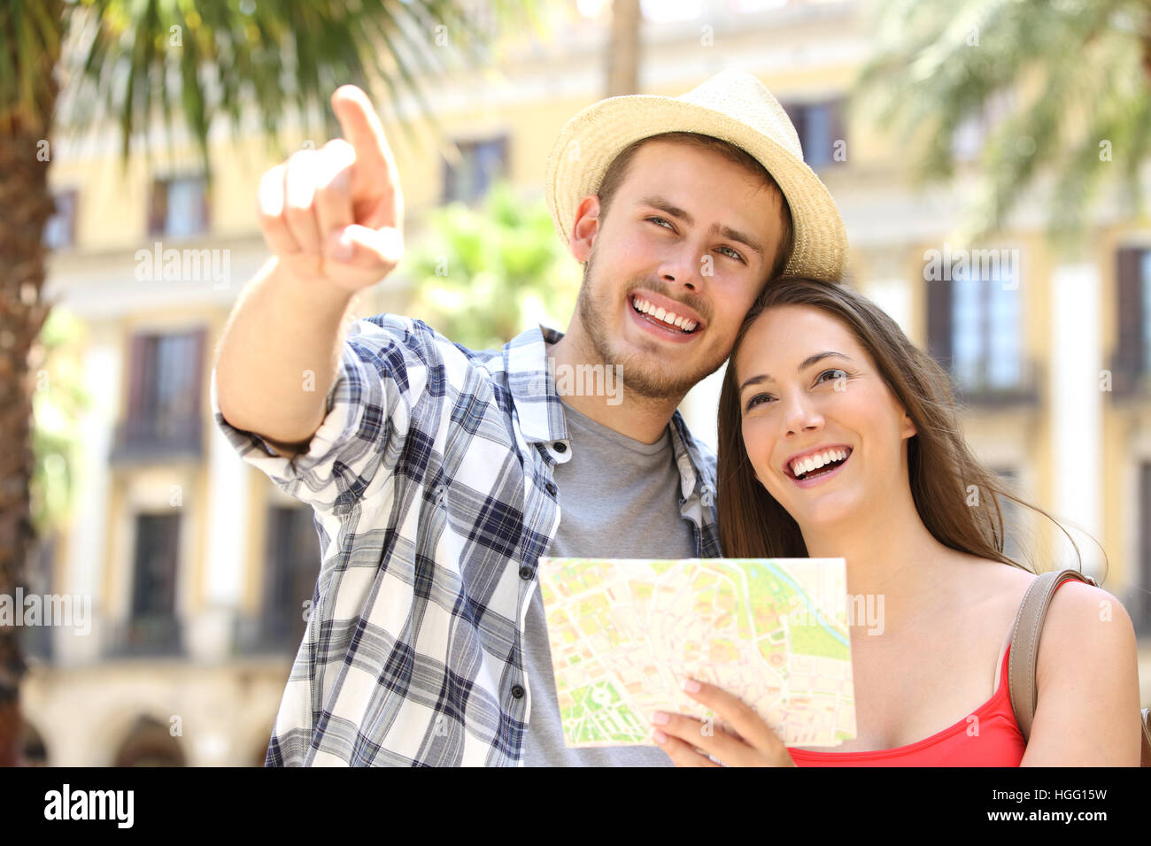 Couple of tourists consulting a guide map in the street of a touristic place during vacations with buildings and palm trees in the background Stock Photo