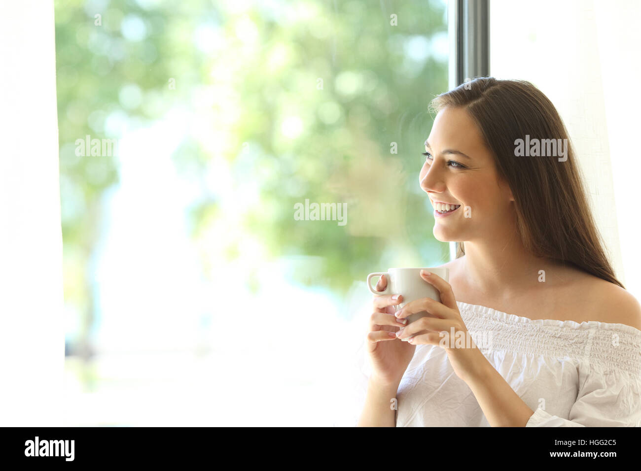 One beautiful girl tasting coffee at home and looking at horizon through a window with a green background outdoors Stock Photo