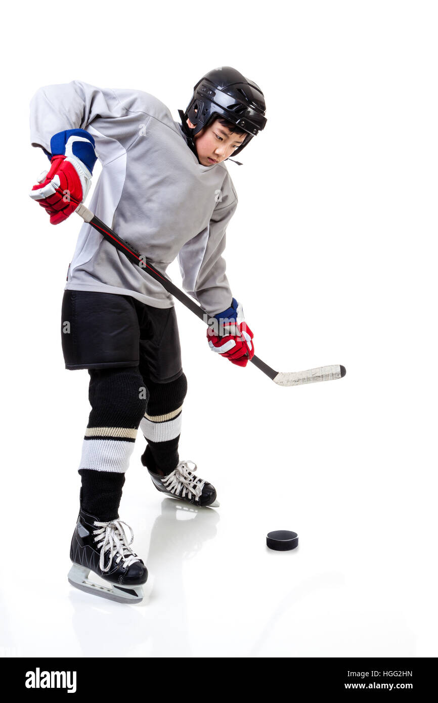 Junior ice hockey player with full equipment and uniform posing for a shot with a puck. Isolated on white background. Stock Photo