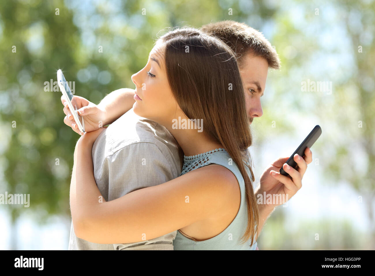 Couple of cheaters hugging and texting everyone on their smart phones Stock Photo