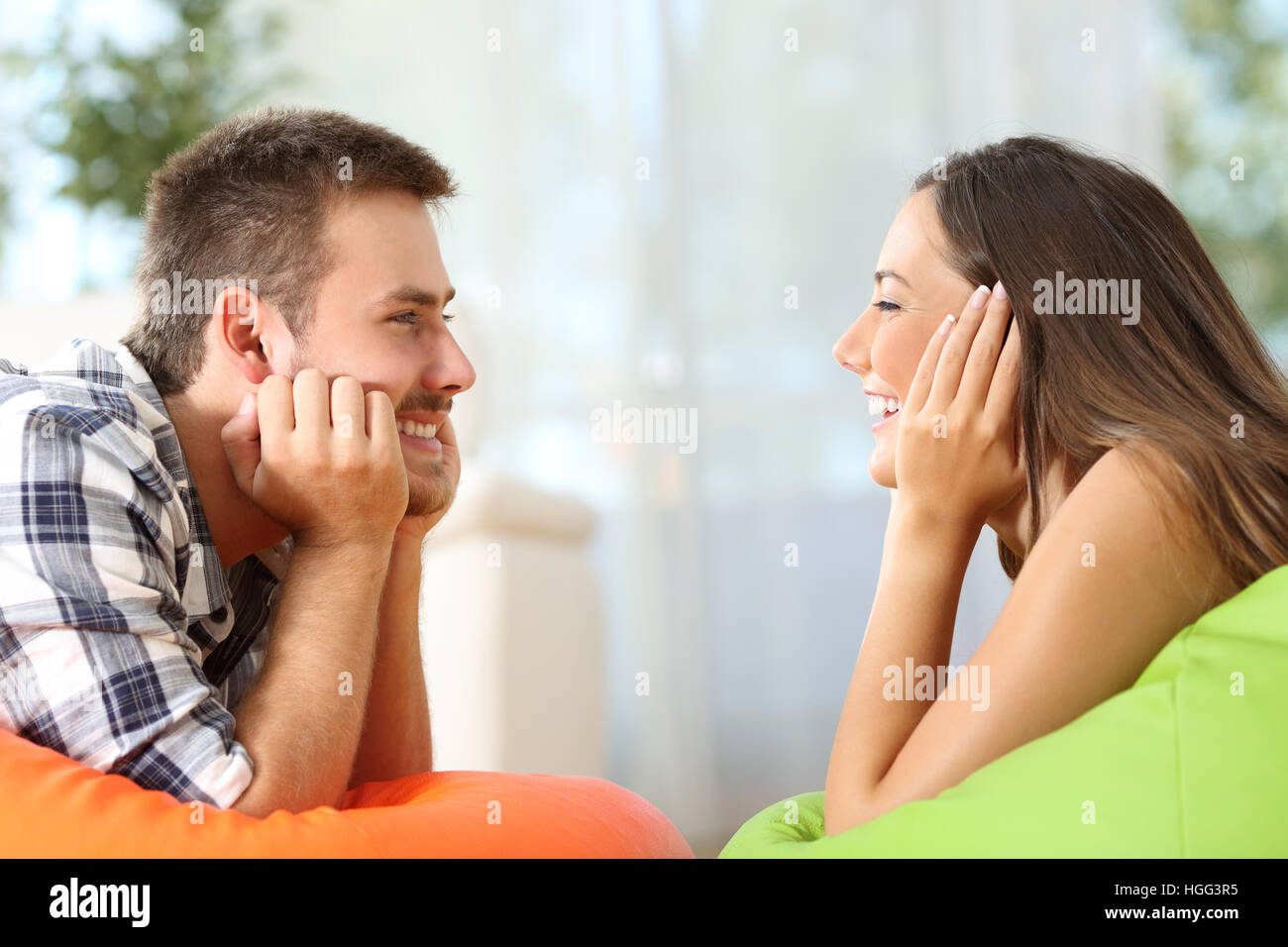 Side view of two friends falling in love looking each other lying on poufs in the living room at home Stock Photo