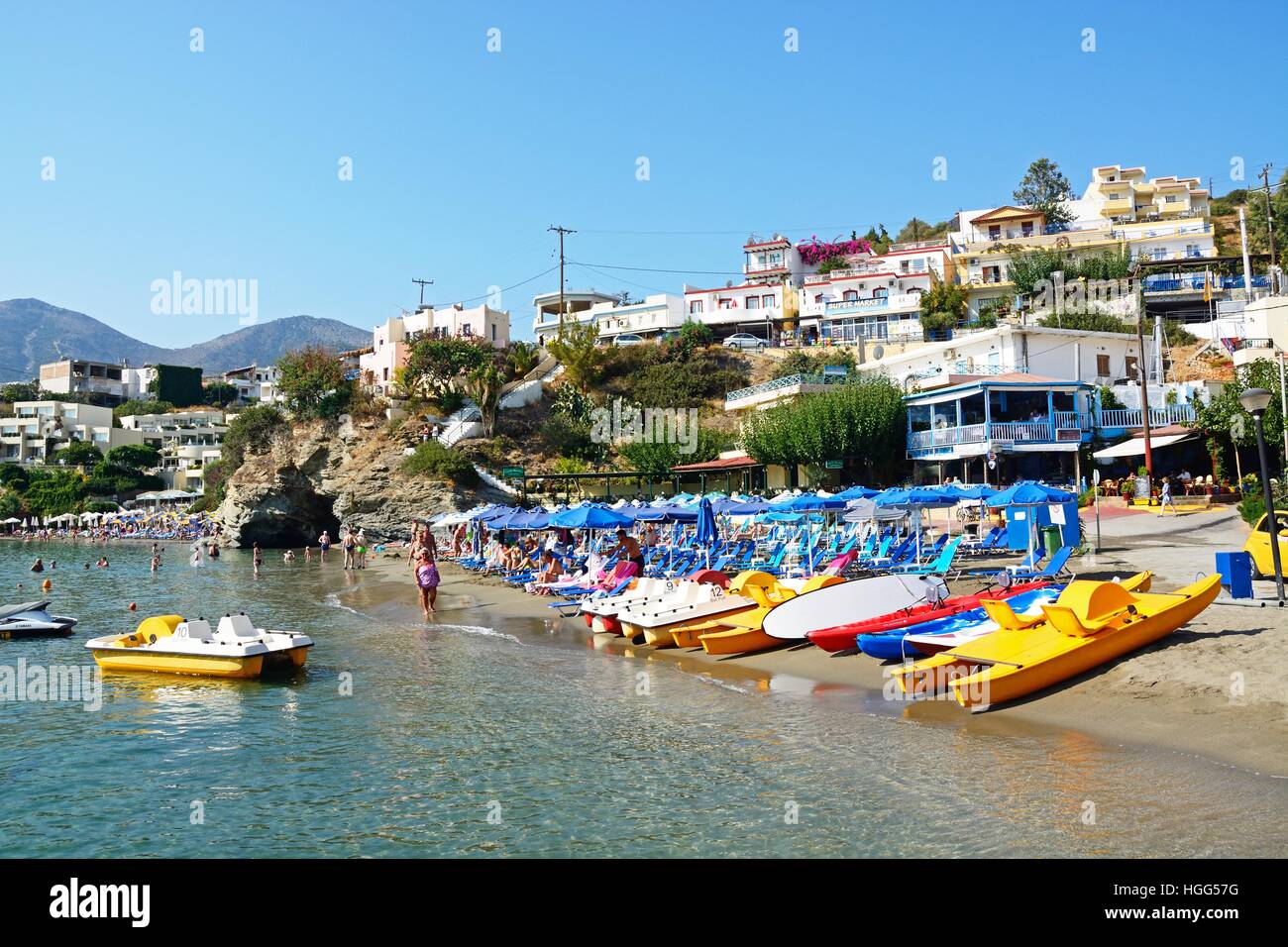 Tourists relaxing on the beach with town buildings to the rear, Bali, Crete, Greece, Europe. Stock Photo