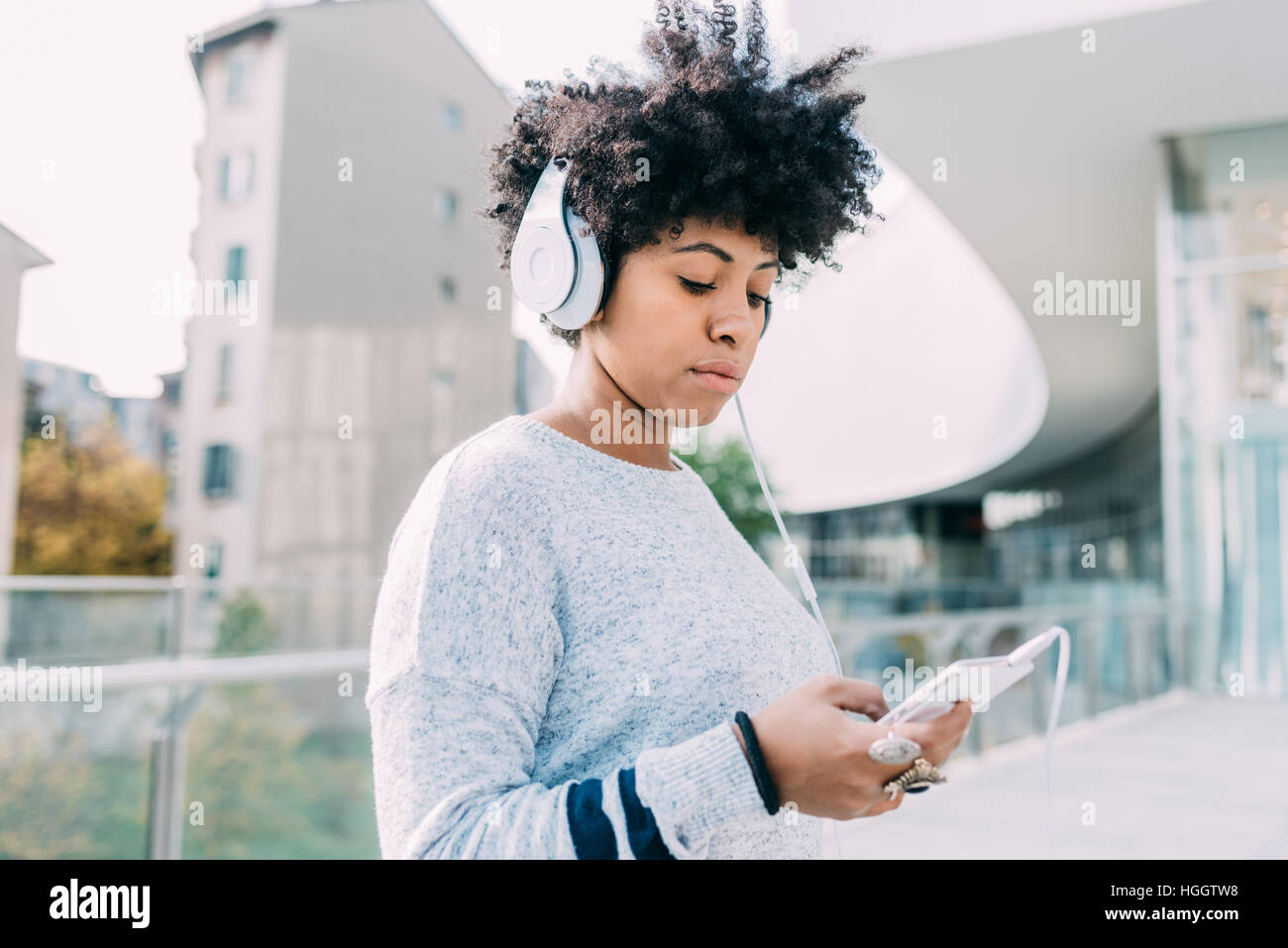Young beautiful afro woman outdoor in city back light listneing music with head phone and smart phone hand hold, thoughtful - melancholic, music, tech Stock Photo