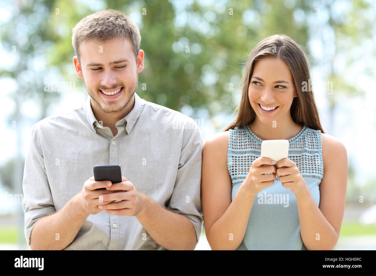 Front view of a couple or friends using smart phones and looking each other askance Stock Photo