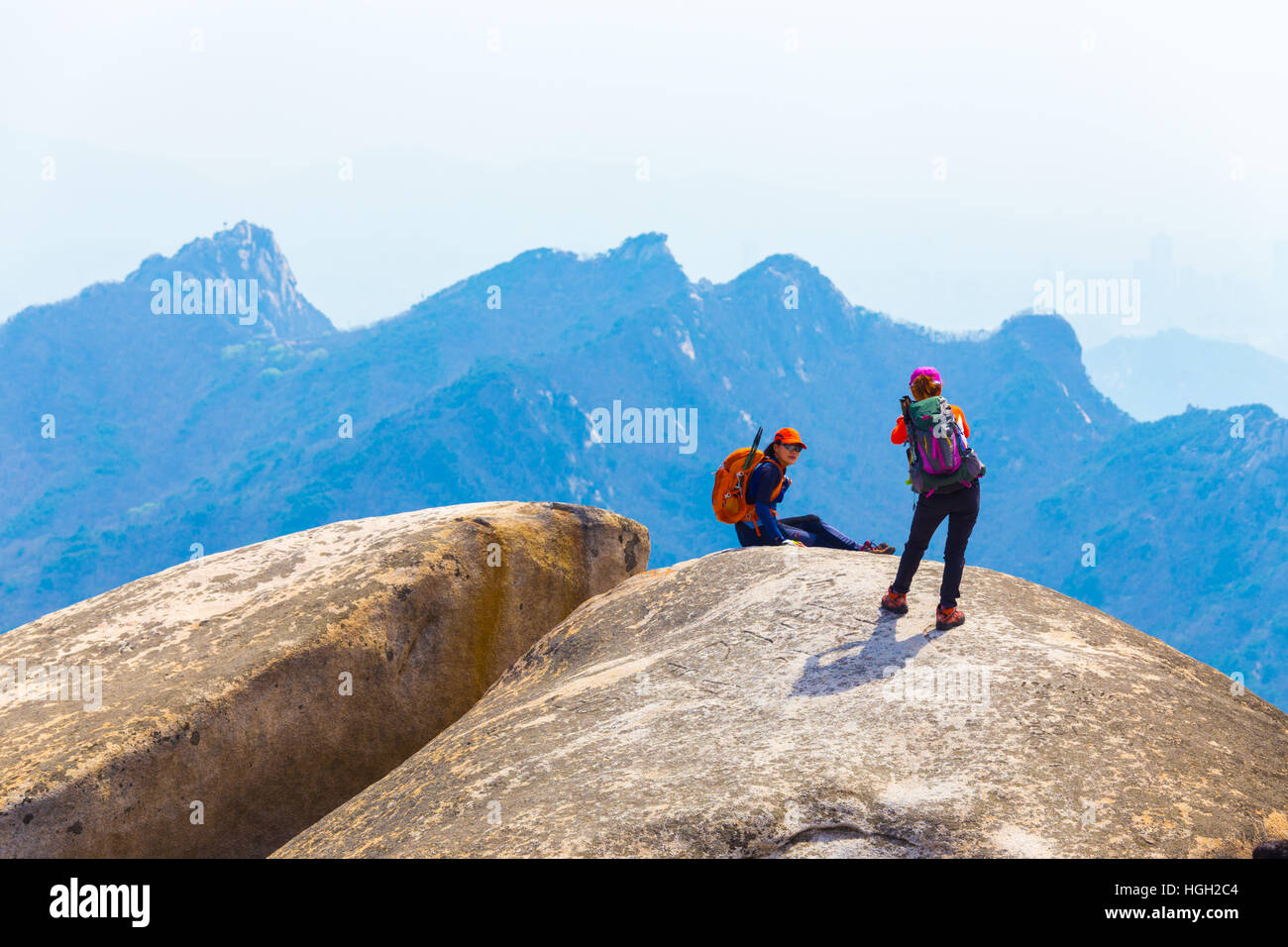 Two Korean women wearing full colorful hiking clothes posing for photos at  Baegundae, peak of Bukhansan mountain on a sunny day Stock Photo