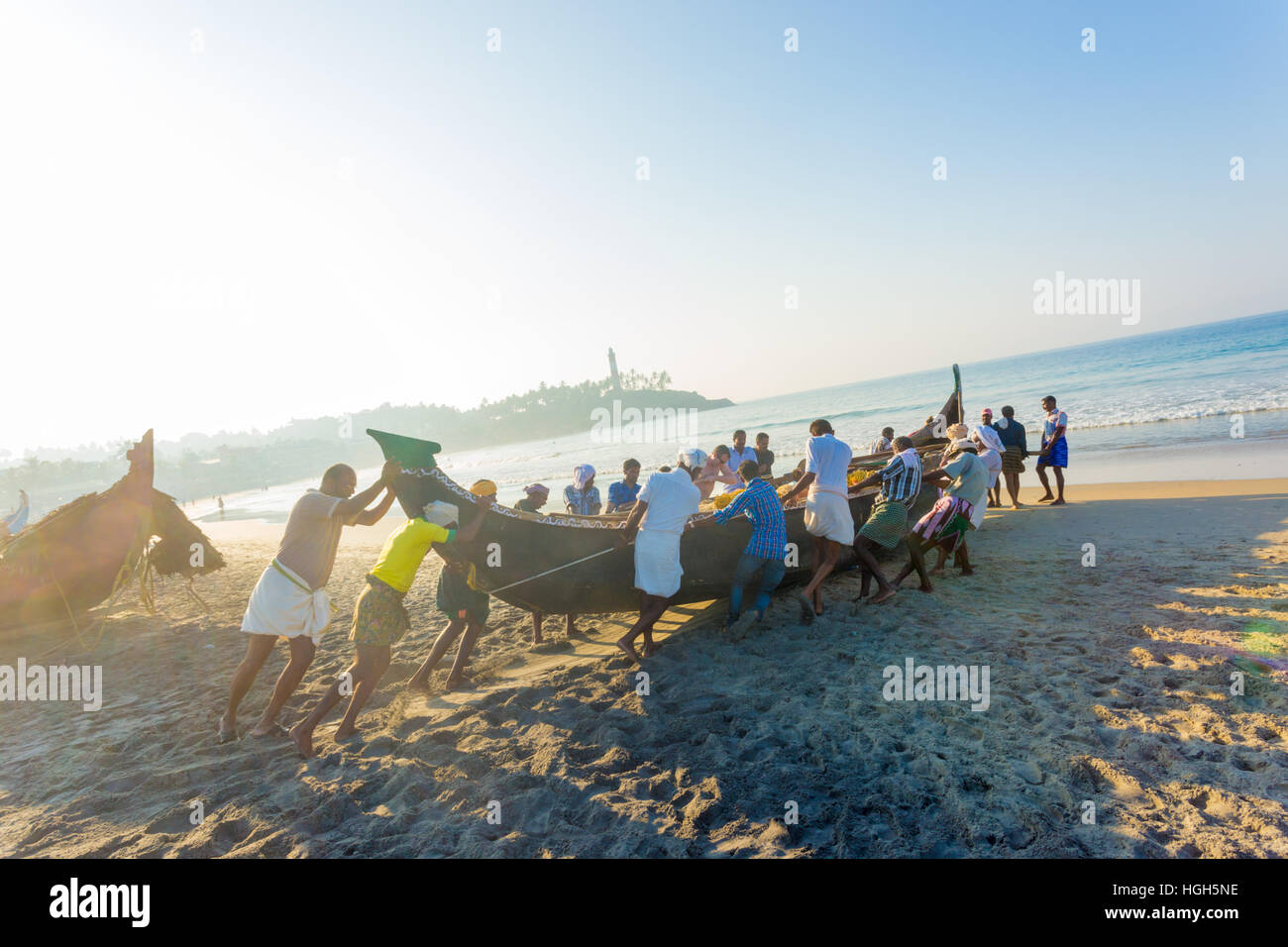 Community helping effort of villagers pushing fishing boat together from sand beach into water on sunny morning in Kovalam India Stock Photo