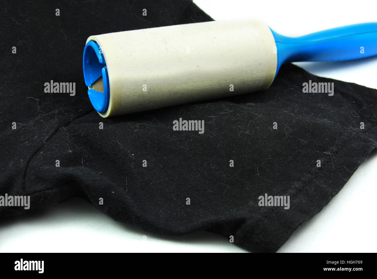 A hand holds a lint brush and removes pet, dog, or cat hair off a black shirt. Stock Photo