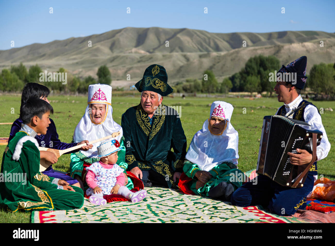 Kazakh family in national costumes sitting in the nature and singing all together. Stock Photo