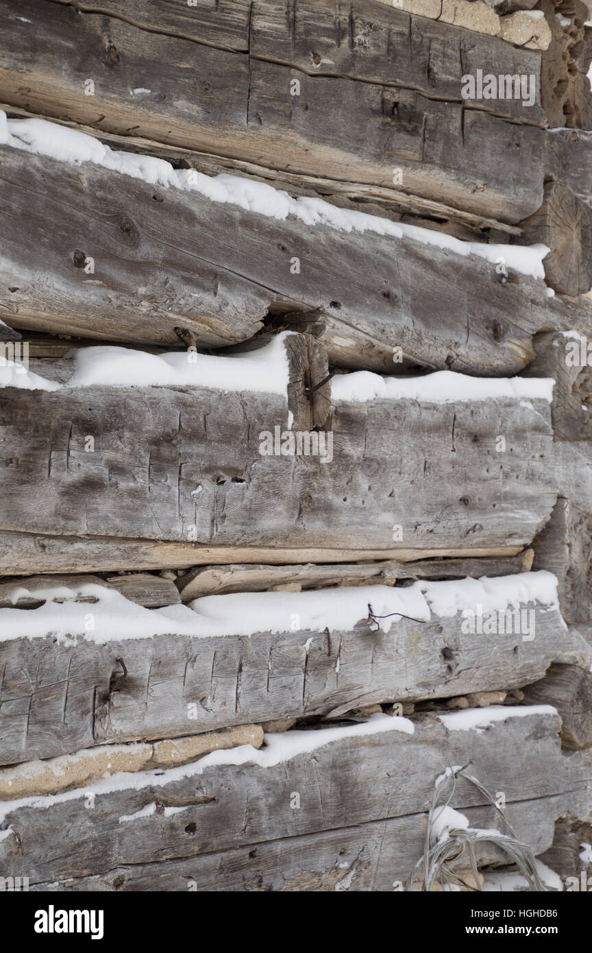 A festive winter background with weathered silvery grey horizontal sawn logs with snow in between.   Logs angle towards the corner of building. Stock Photo