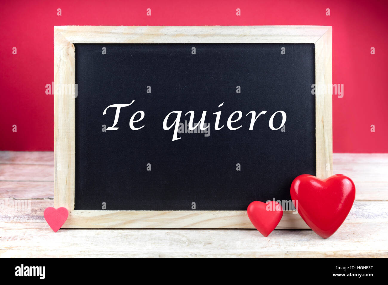 Wooden blackboard with red hearts and written sentence in Spanish 'Te quiero', which means 'I love you', in red background. Stock Photo