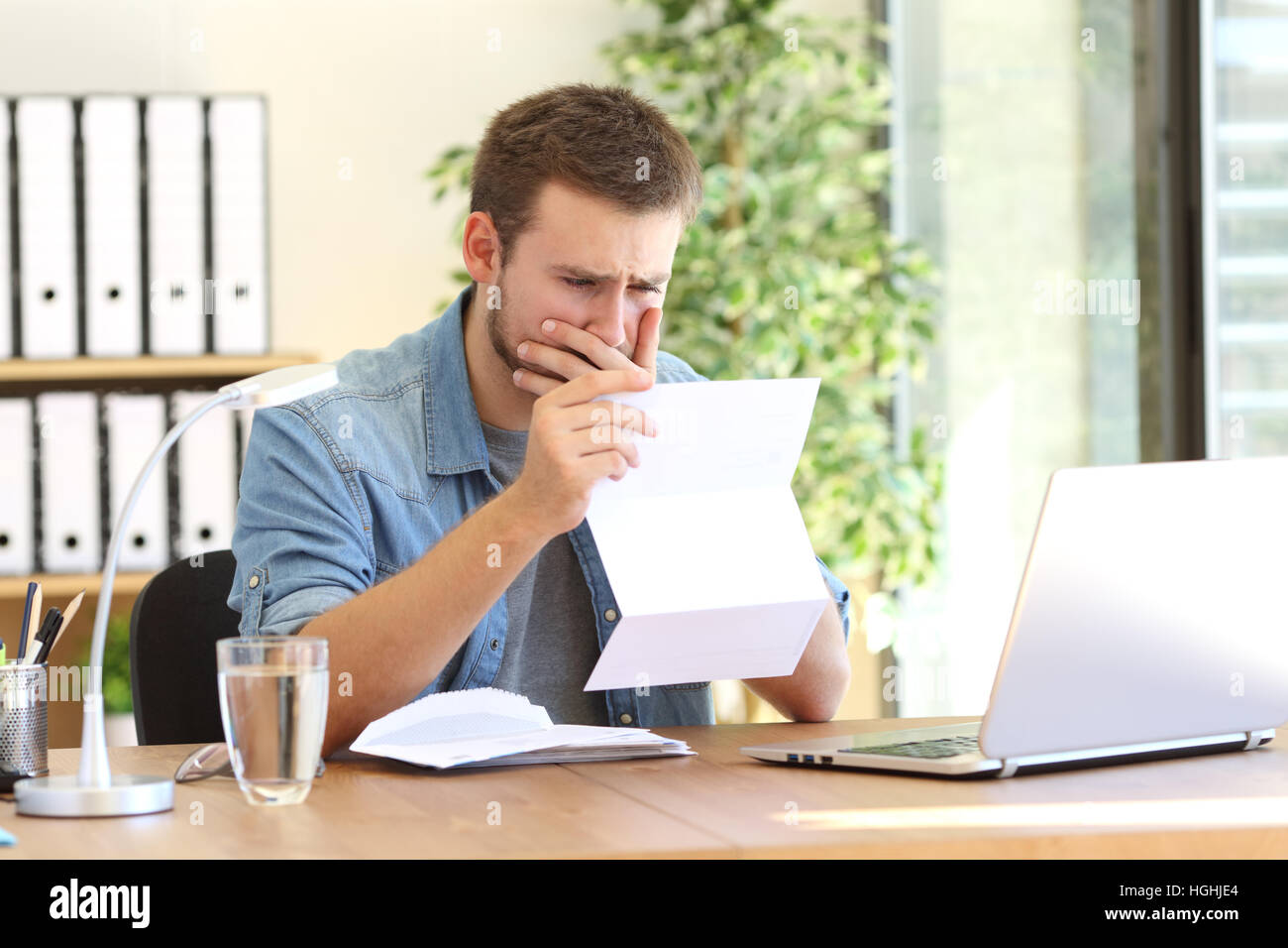 Worried entrepreneur working and reading a letter with bad news in a desk at office Stock Photo