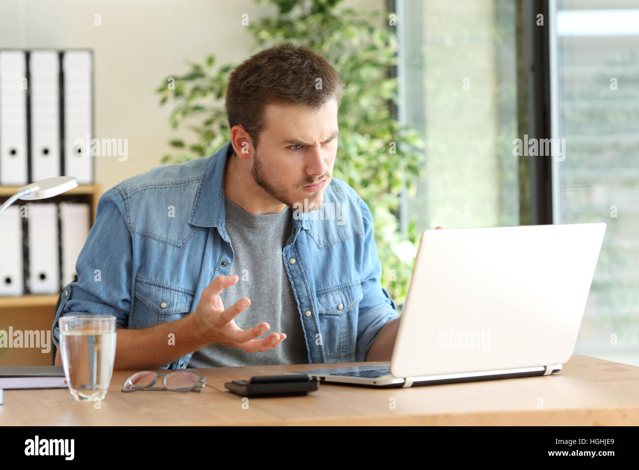 Angry freelance professional having problems on line with a laptop in a desktop beside a window at office Stock Photo