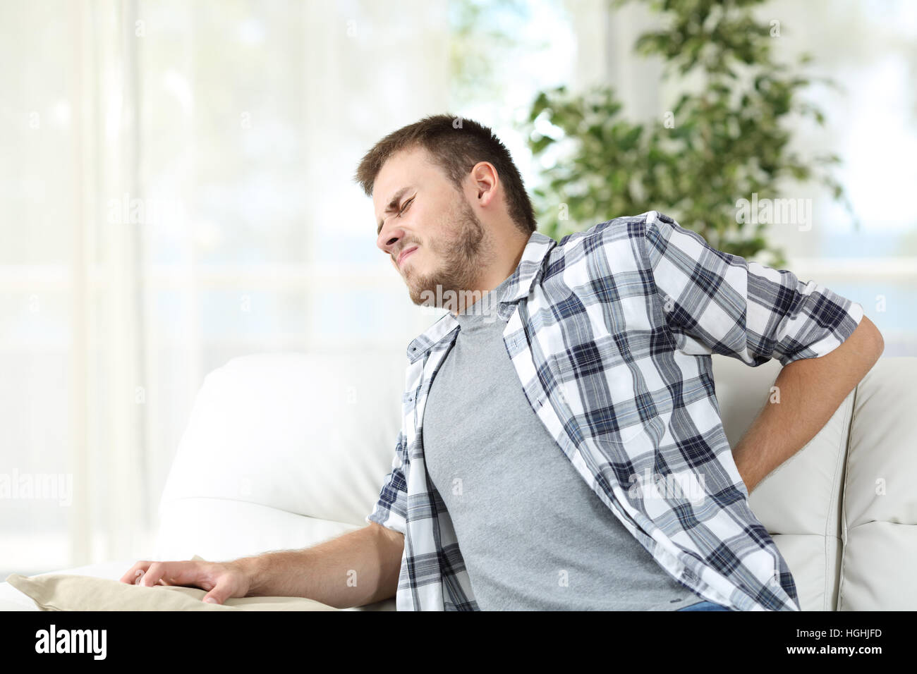 Unhappy man suffering back pain sitting on a sofa in the living room at home Stock Photo