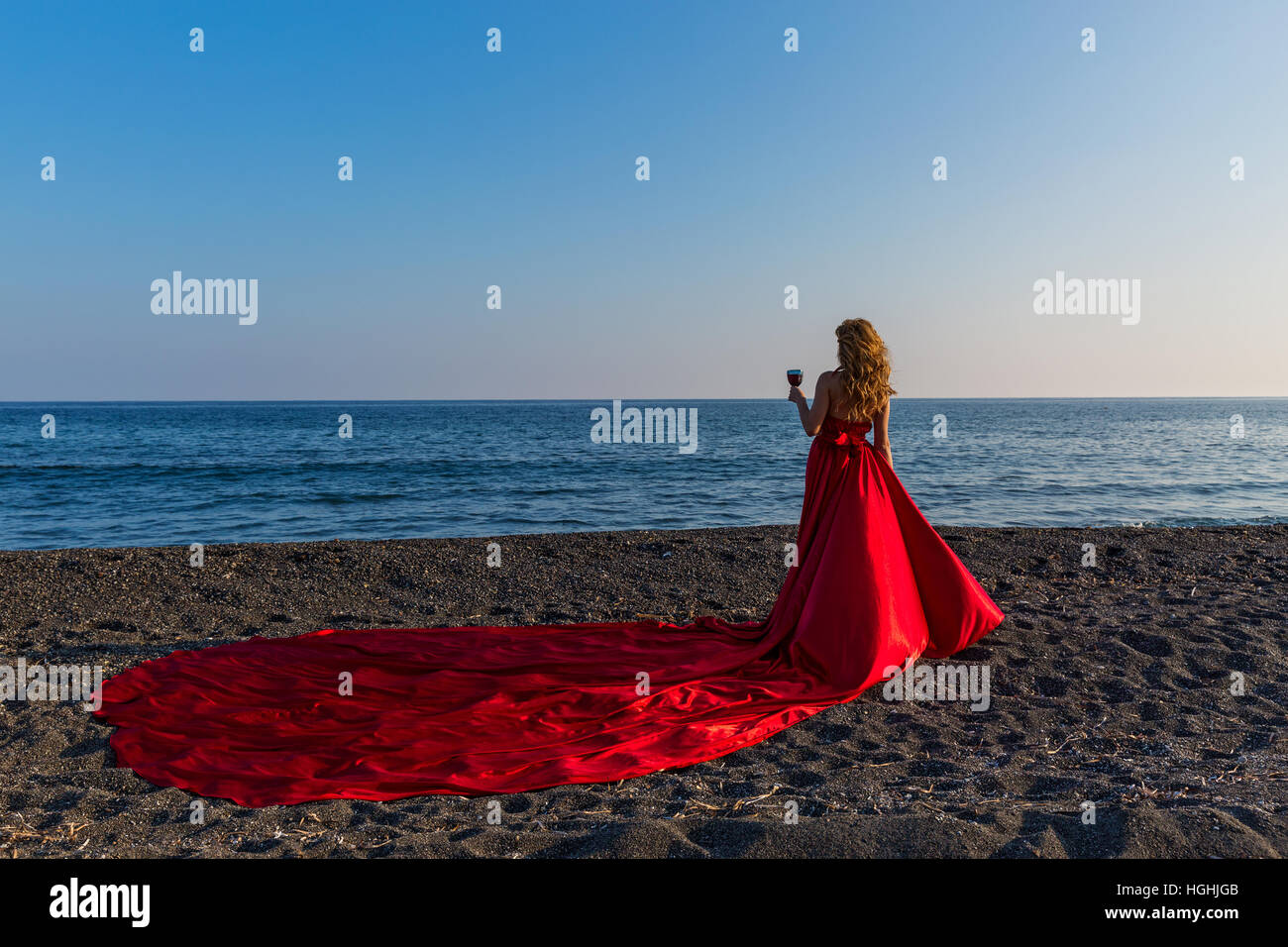 Beautiful woman in red dress and Santa hat is on the shore of the sea ...