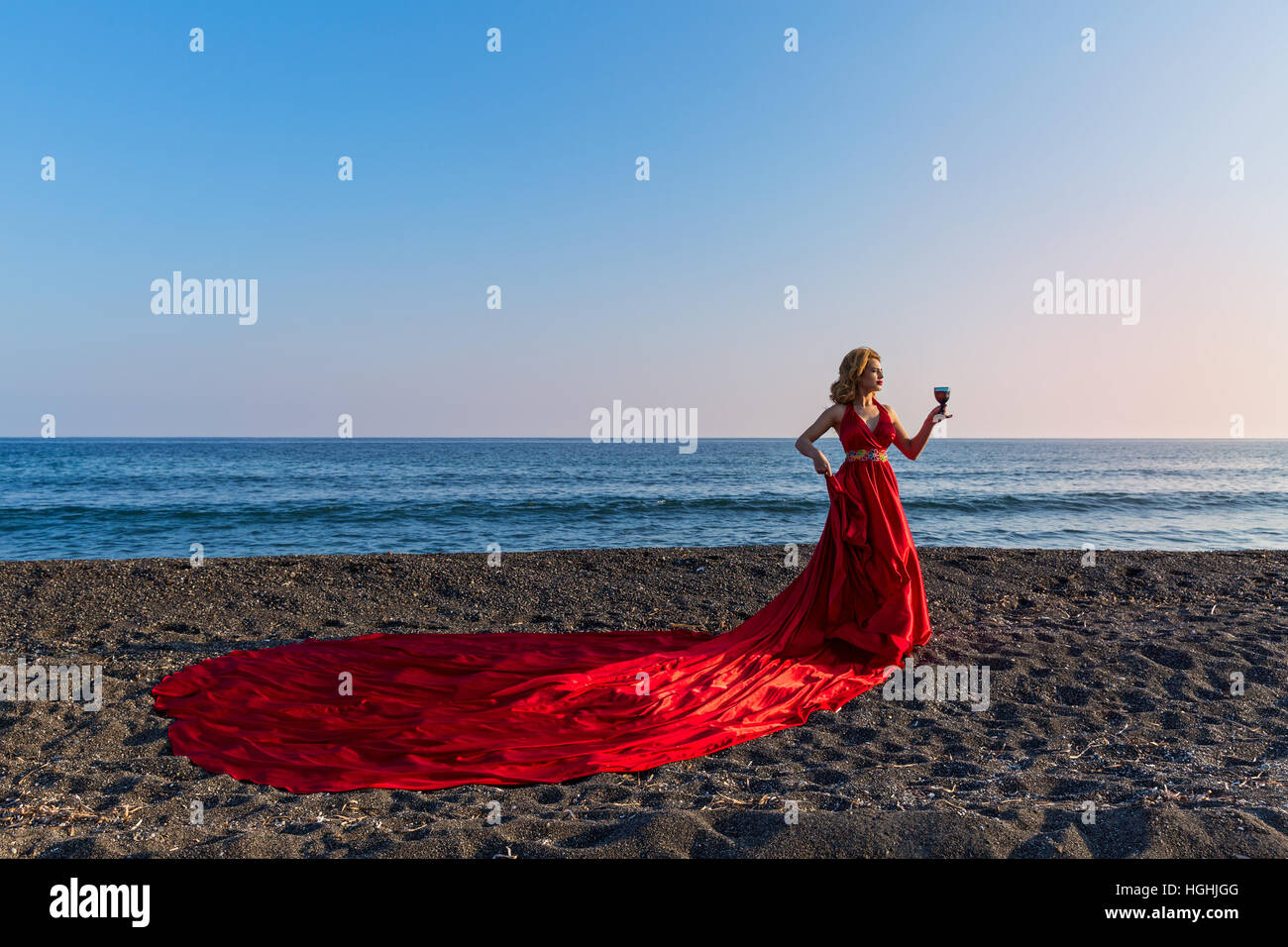 Beautiful woman in red dress and Santa hat is on the shore of the sea ...