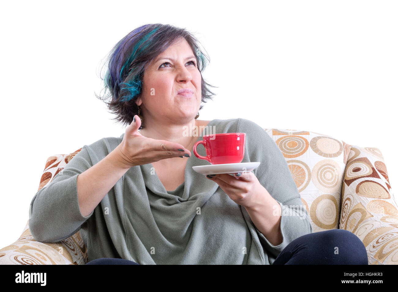 Grimacing woman sat in chair gesturing unhappily at cup of coffee or coffee, white background Stock Photo