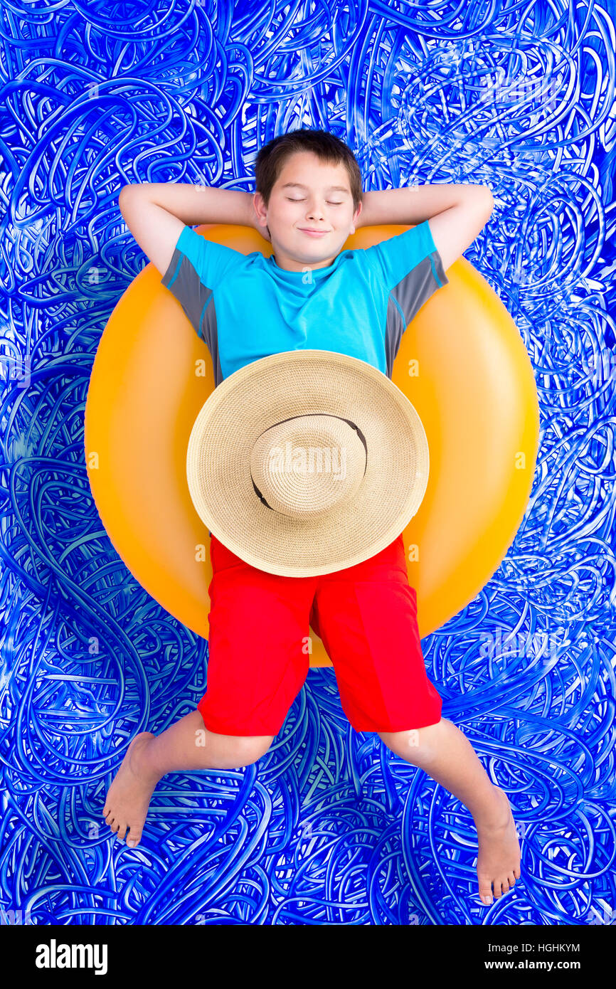 Handsome little boy dozing off in the swimming pool relaxing on a bright yellow tube with closed eyes and a blissful smile, conceptual image on blue p Stock Photo