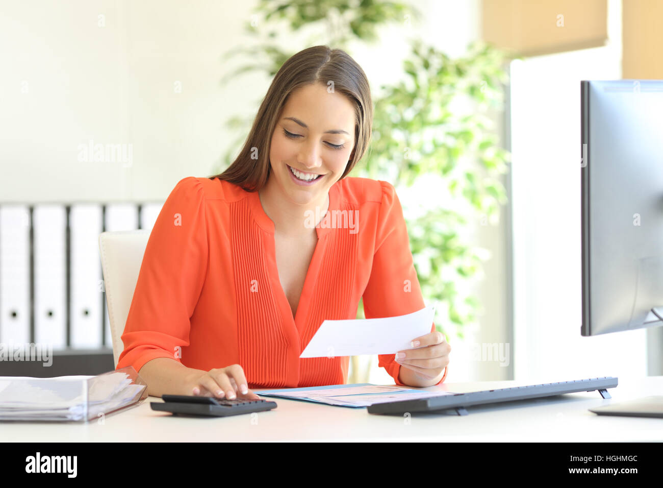 Businesswoman wearing orange blouse doing accounting and calculating with a calculator in a desktop at office Stock Photo