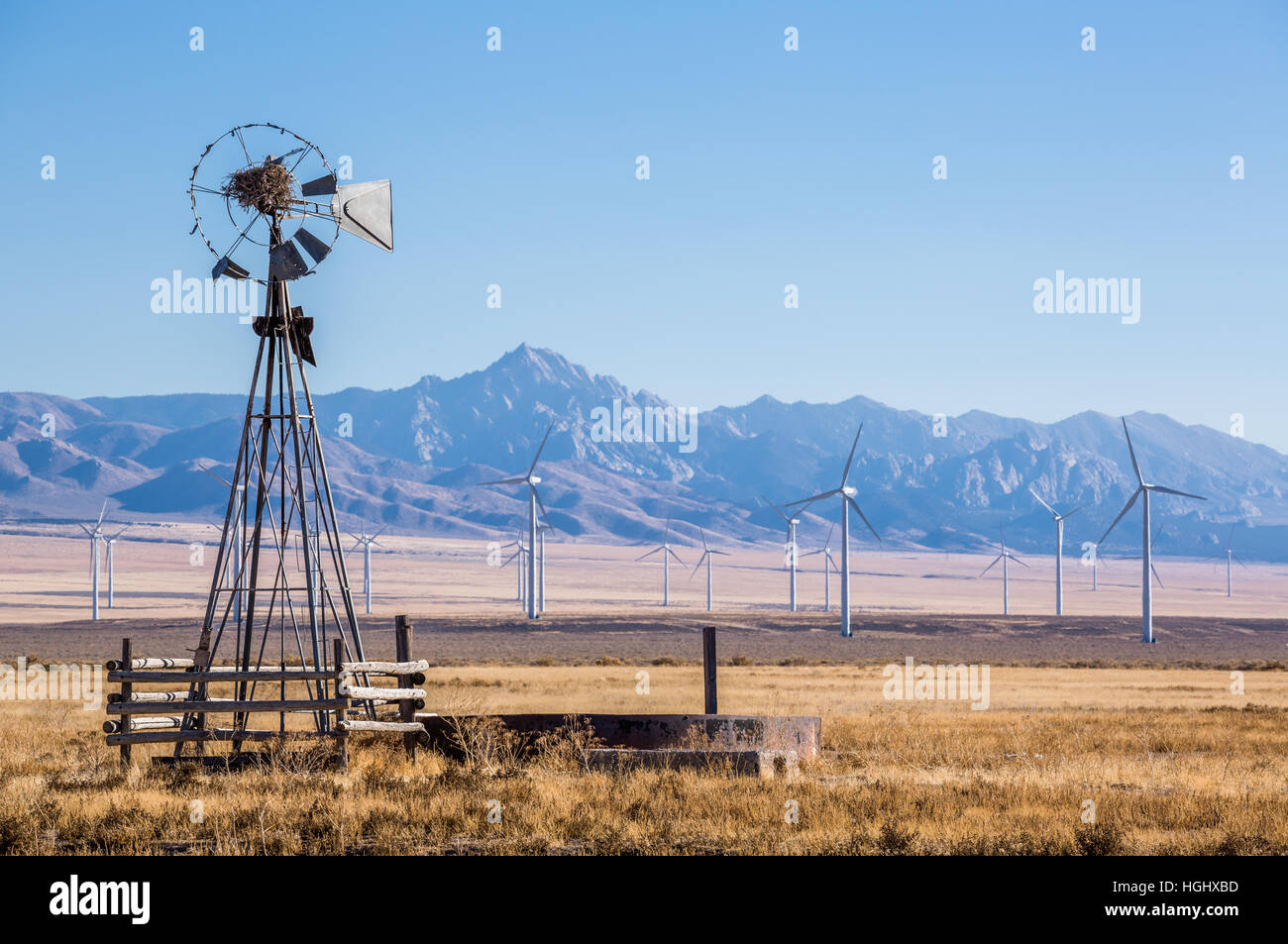 Old, windmill that is falling apart and now has a large bird nest on it rests in front of a large windfarm with 23 visible wind turbines Stock Photo