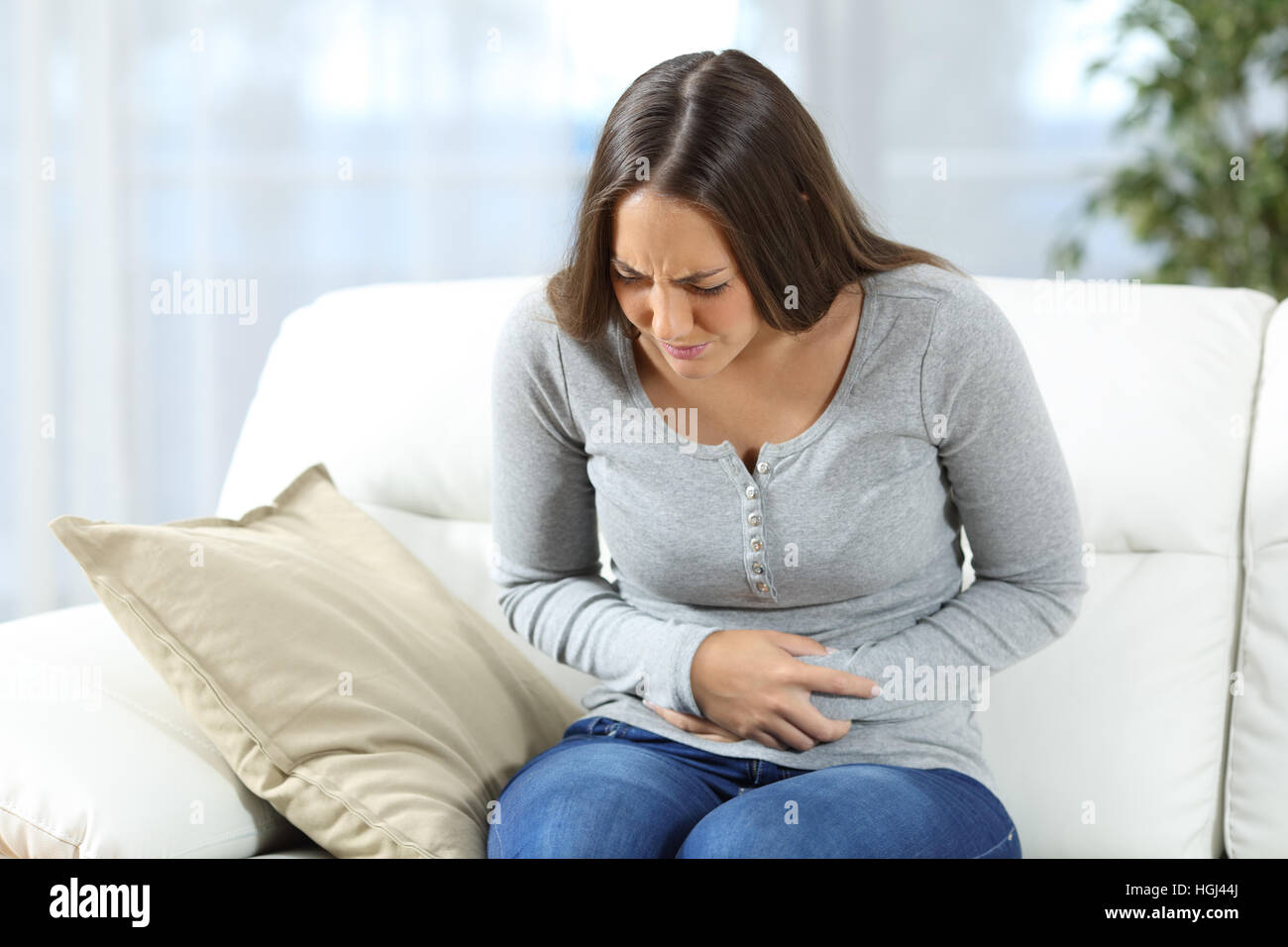 Woman suffering stomach ache and complaining sitting on a couch in the living room at home Stock Photo