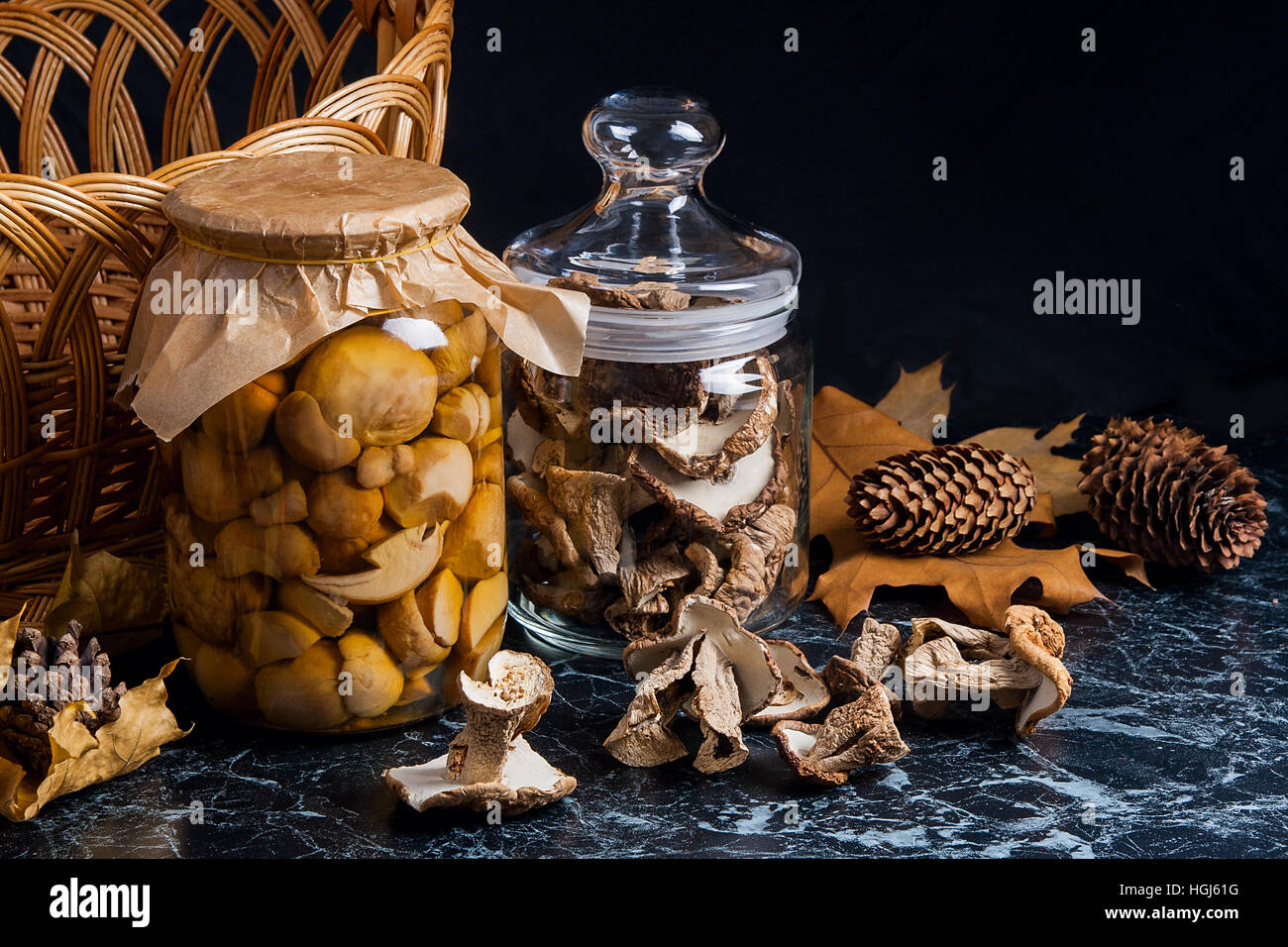 Two glass jars with wild mushrooms on black marble background. One jar