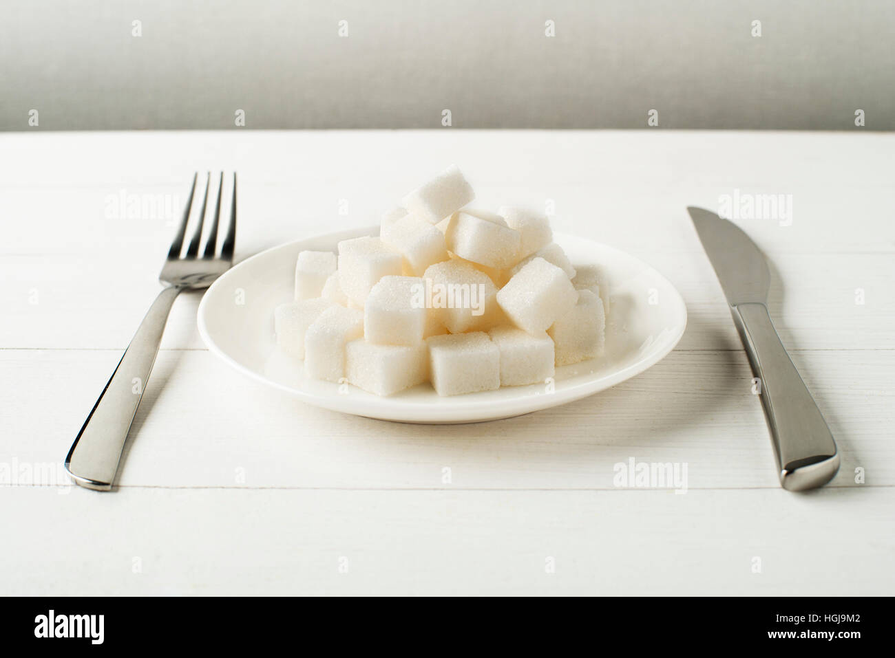 Junk-food, diet and unhealthy eating concept - close up of sugar on plate with knife and fork Stock Photo