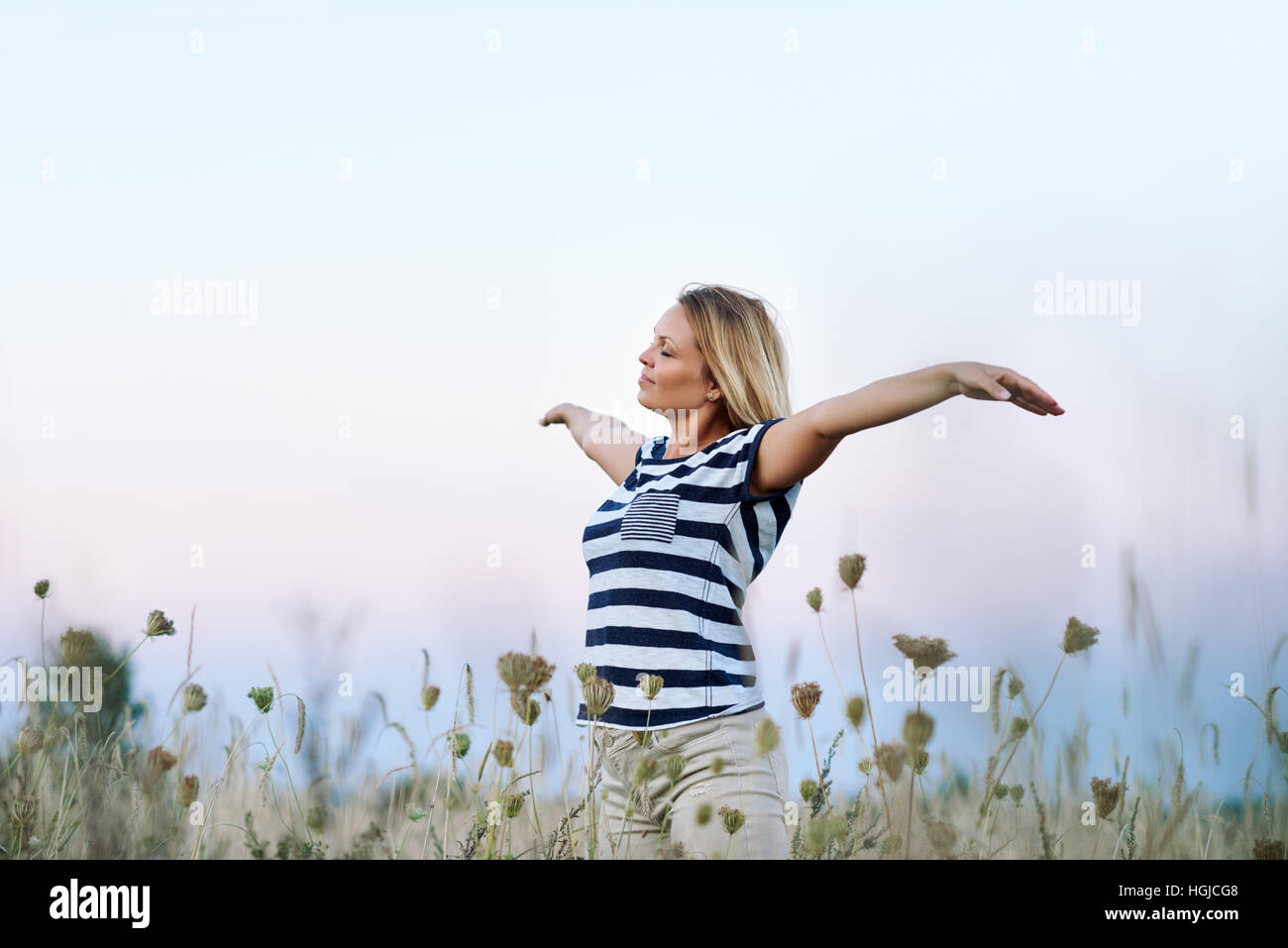 Young woman raising her arms to the blue sky Stock Photo