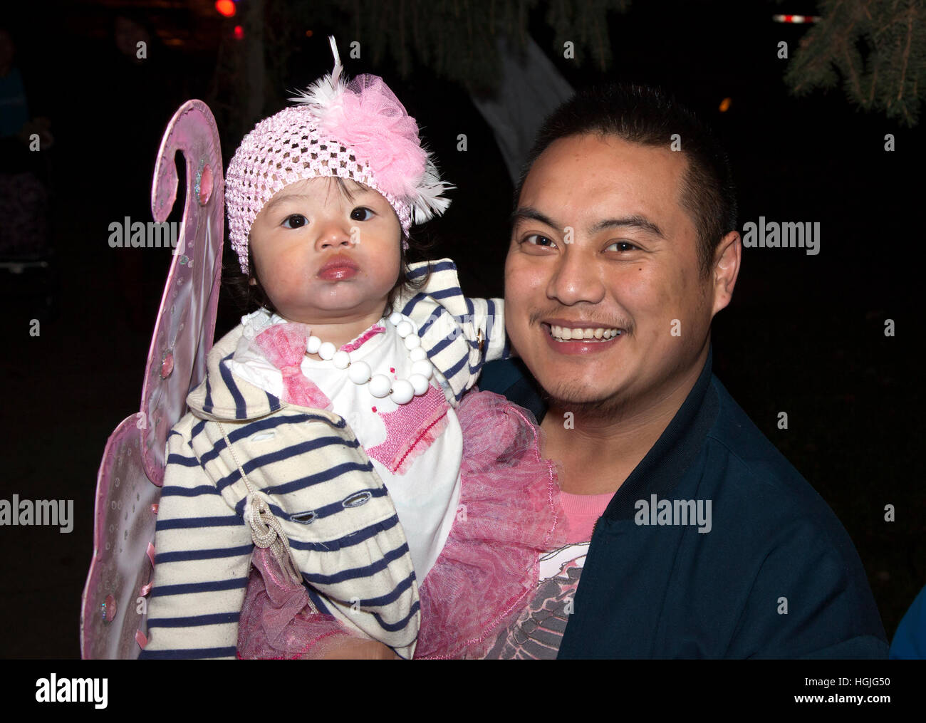 Happy Asian American father carrying his costumed baby out for a Halloween trick or treat evening. St Paul Minnesota MN USA Stock Photo
