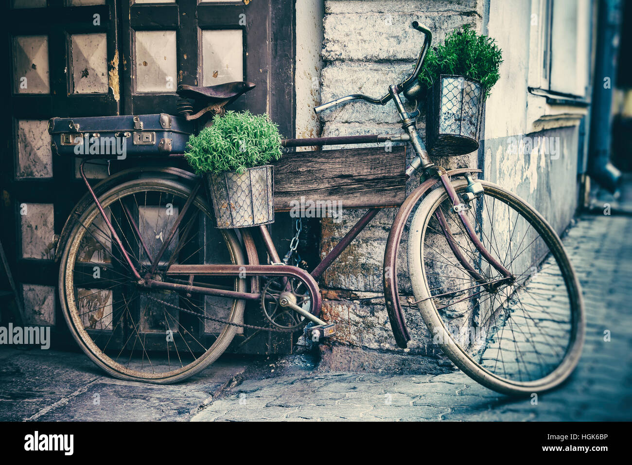 Vintage stylized photo of old bicycle carrying flower pots and suitcase as decoration and wooden plank for writing the text inside Stock Photo