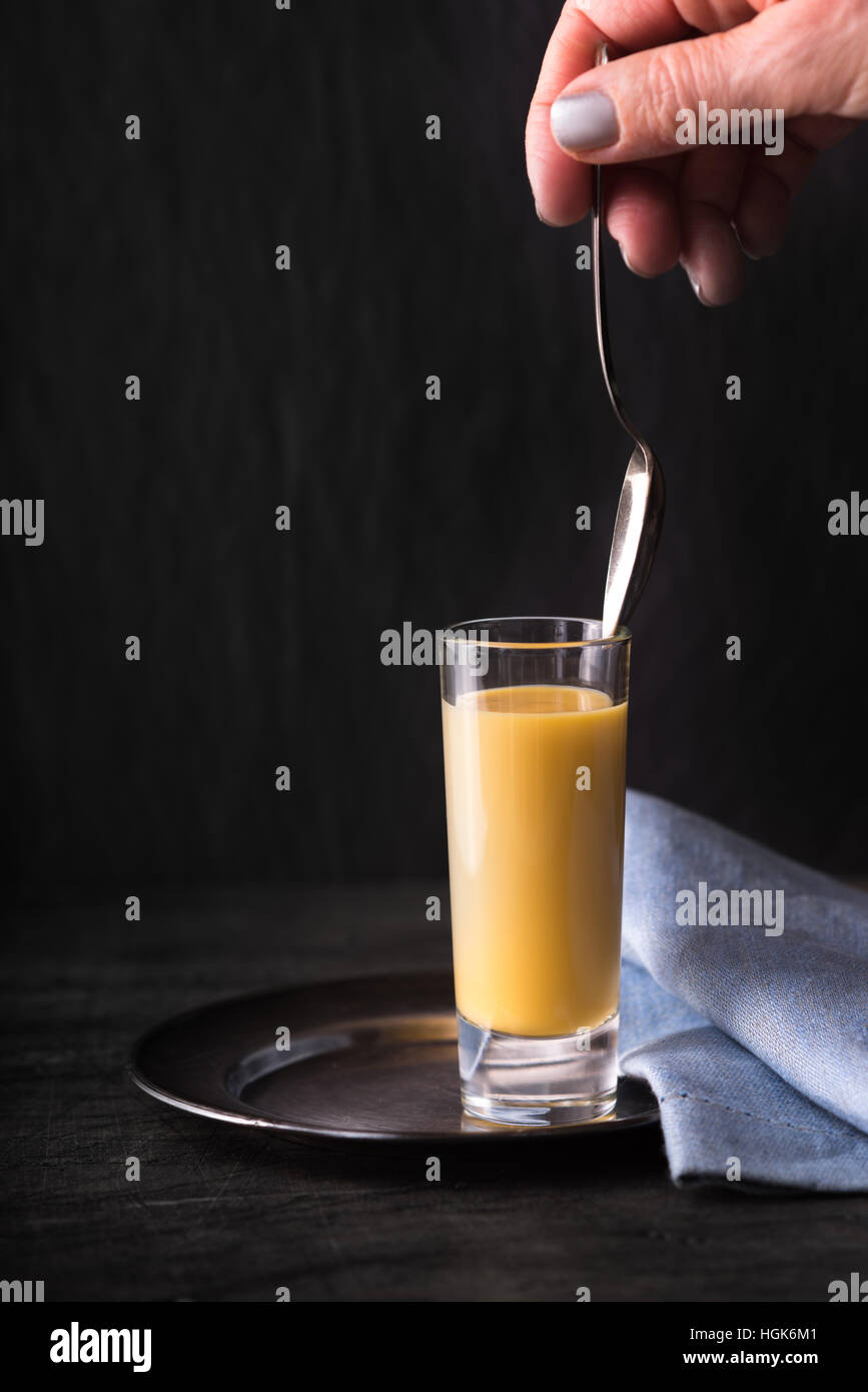 Egg liqueur  in the glass with spoon in the hand vertical Stock Photo