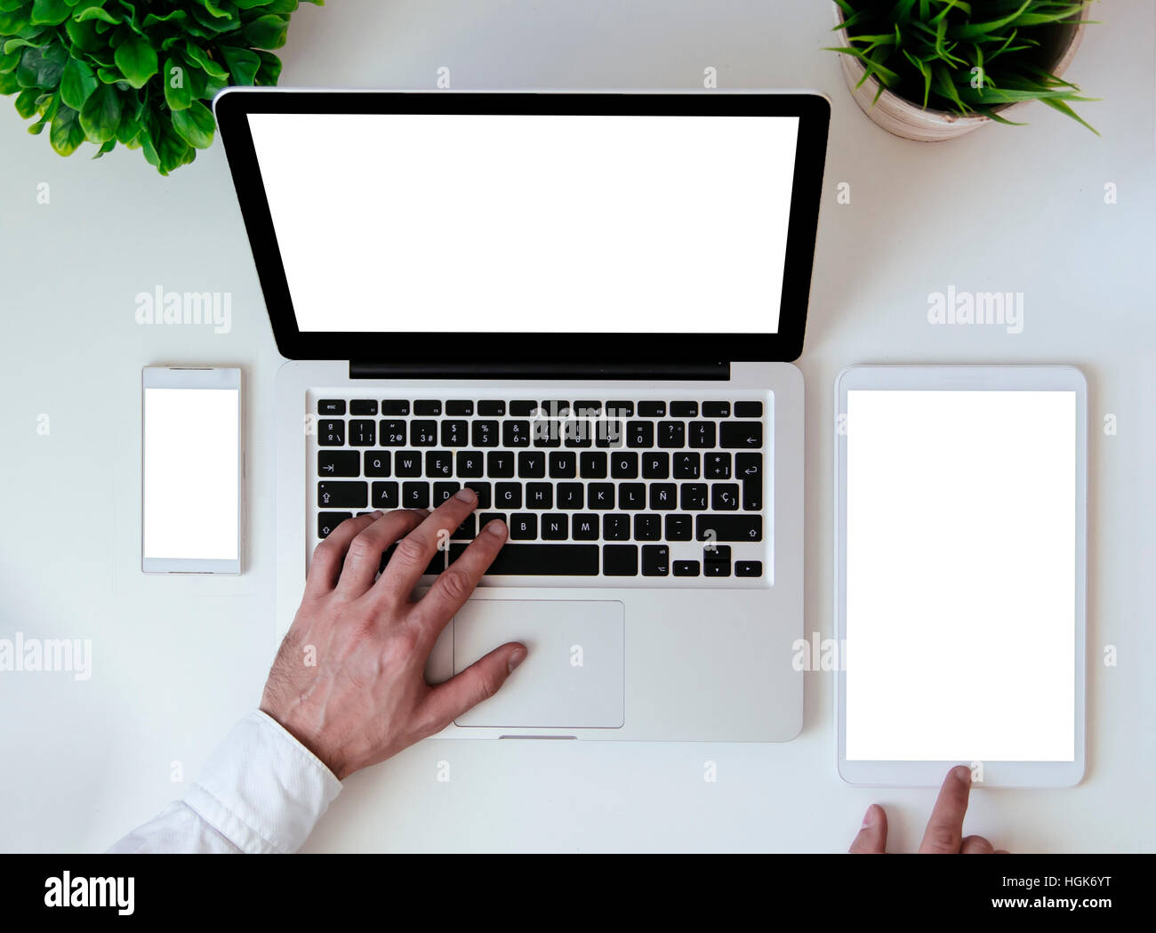 office tabletop with tablet, smartphone and laptop showing white screen