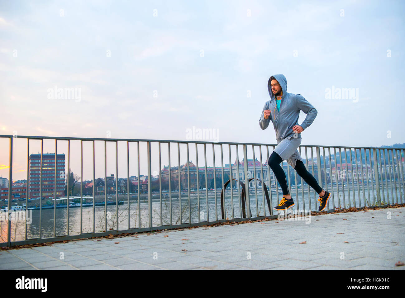 A handsome young man running in the sunset next to a fence on the