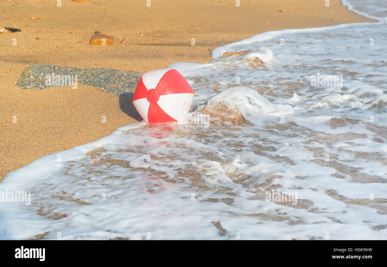 Red and white beach ball playing with the surf and the sea at the beach