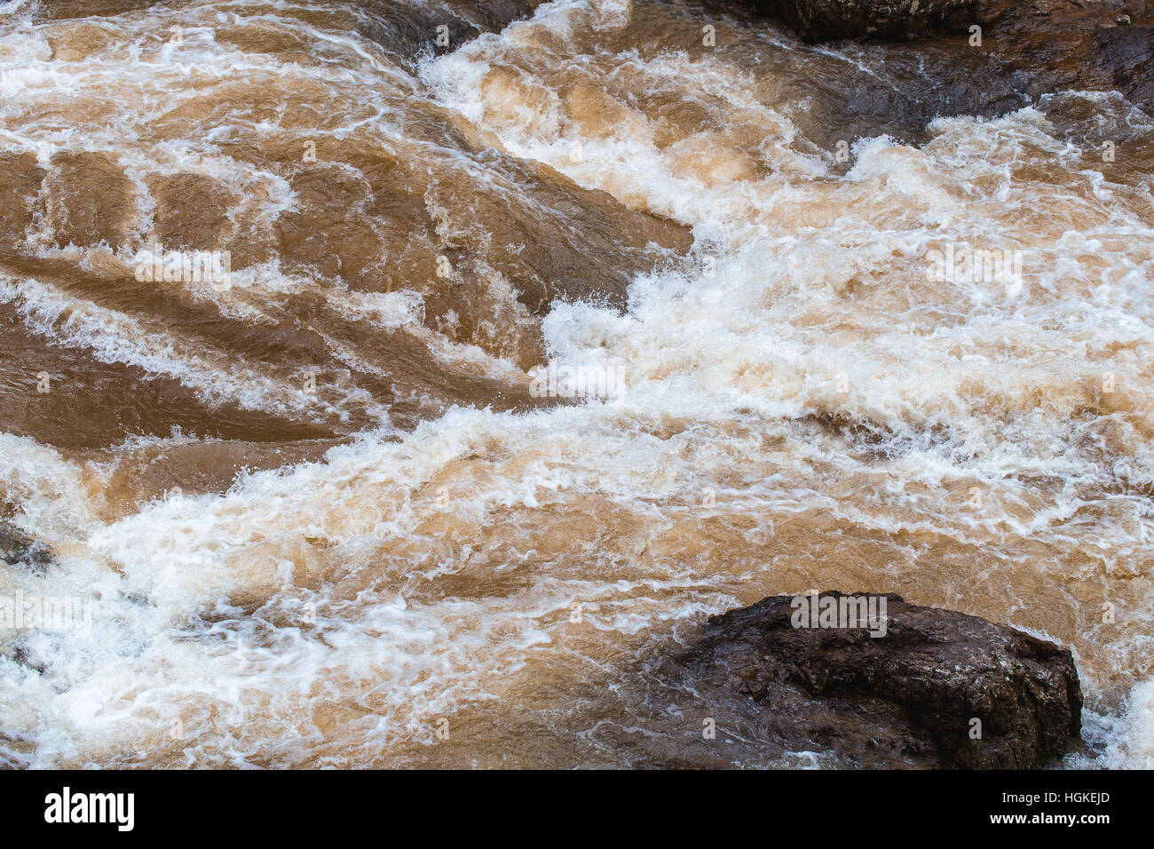 Close focus on wave of mud water flowing through rock river after raining inside tropical forest Stock Photo