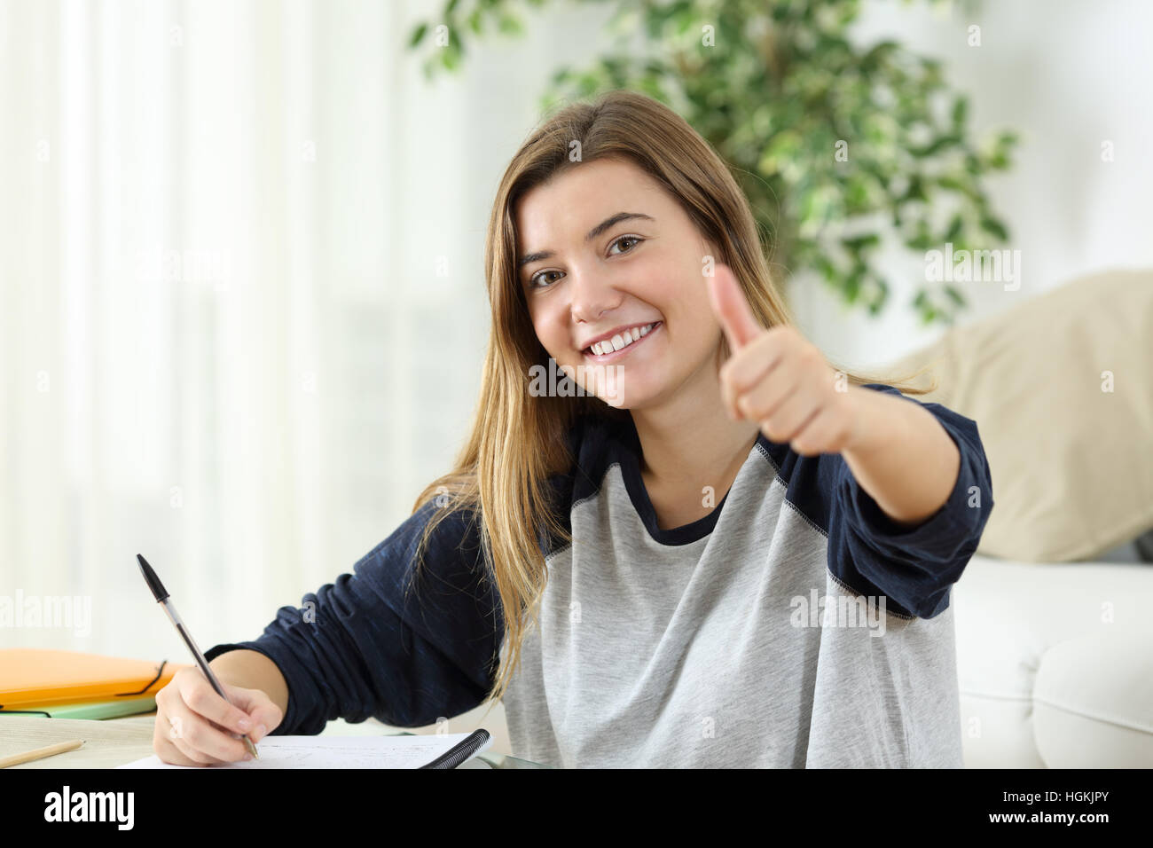 Happy student looking at you with thumbs up sitting on the floor of the living room at home Stock Photo