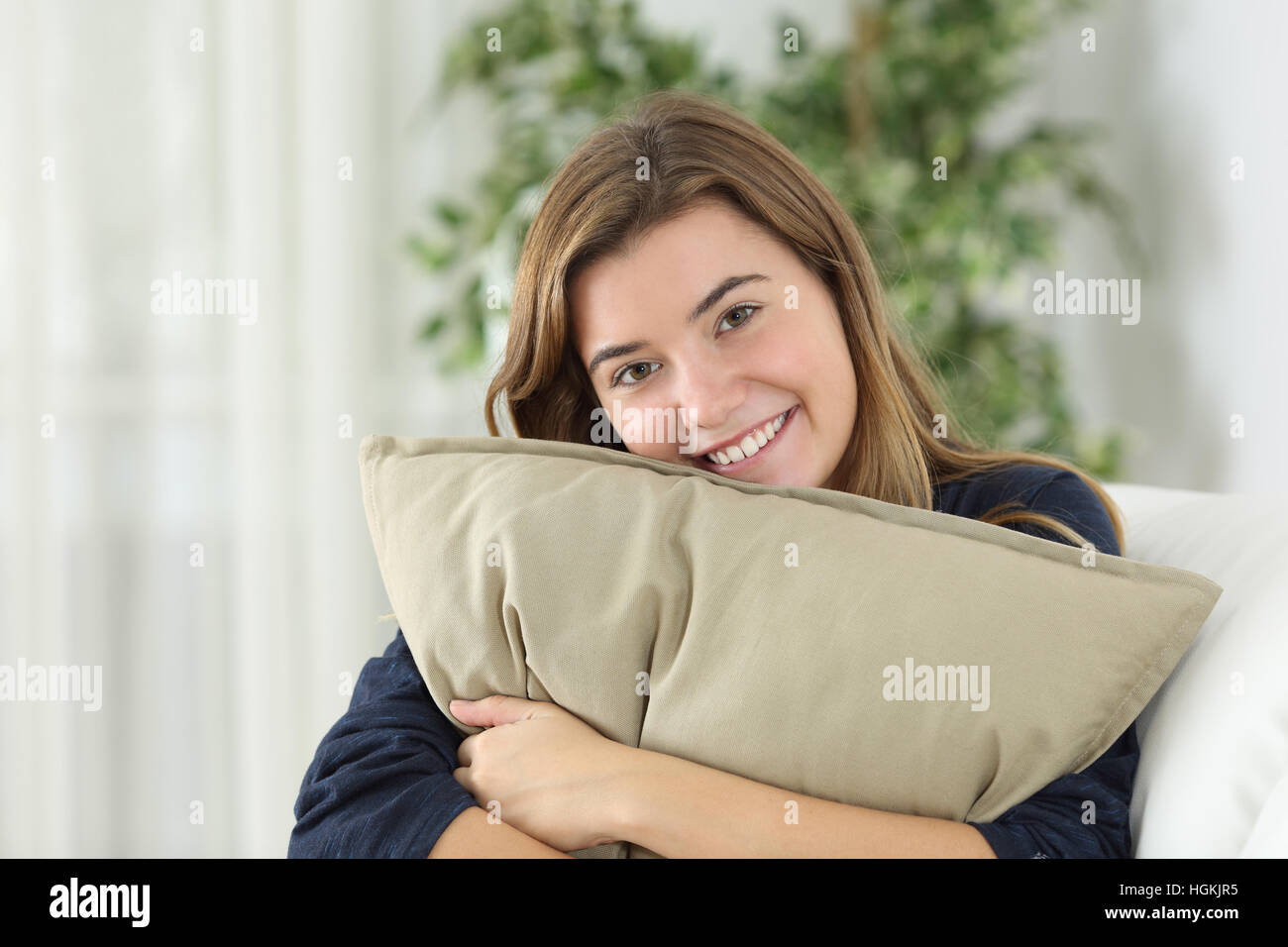 Happy teen girl posing looking at you sitting on a couch in the living room at home Stock Photo
