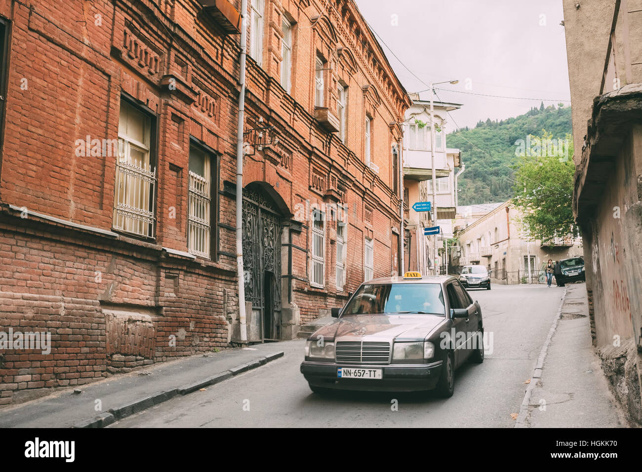 Tbilisi, Georgia - May 20, 2016: The View Of Moving Gray Mercedes Benz, Taxi Car On Narrow Besik Street Between Old Buildings In Spring Day Under Somb Stock Photo