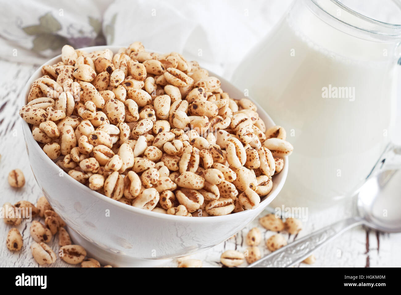 Puffed wheat cereal in white bowl with pitcher of milk in background Stock Photo