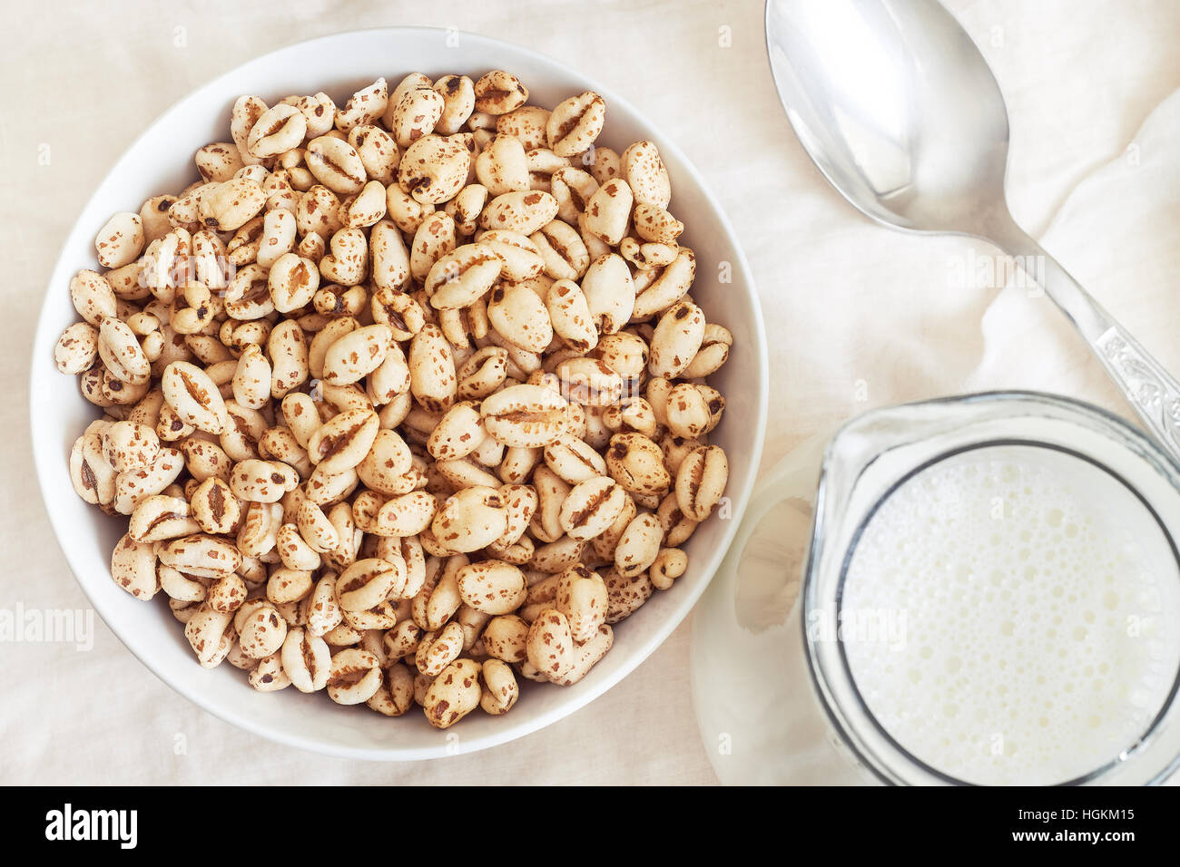 Puffed wheat cereal in white bowl with pitcher of milk and spoon. Top view Stock Photo