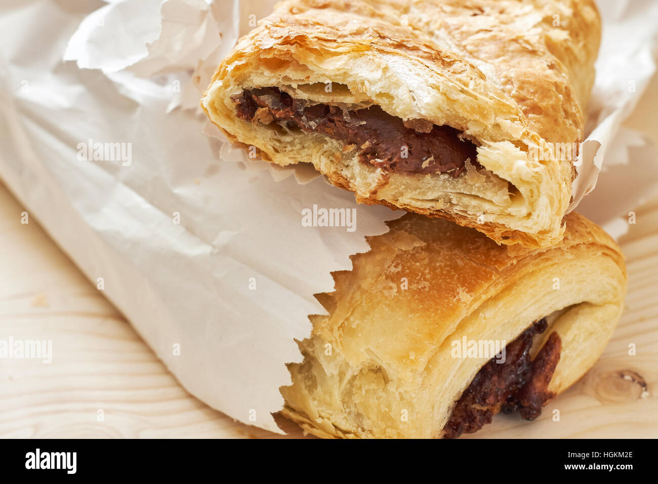 Puff pastry with chocolate filling in white paper bag on wooden background Stock Photo