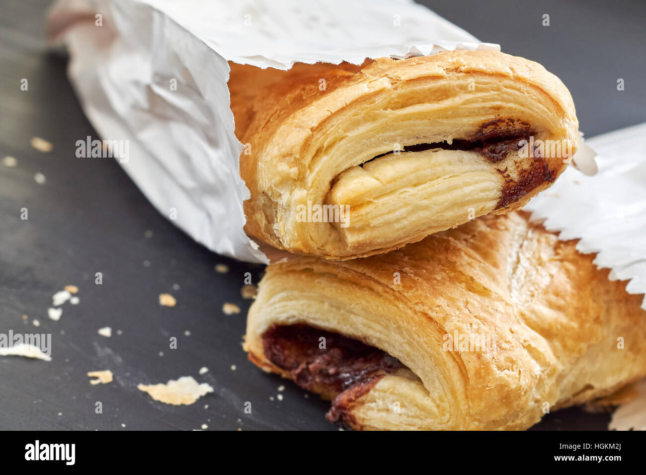 Puff pastry with chocolate filling in white paper bag on black wooden background Stock Photo