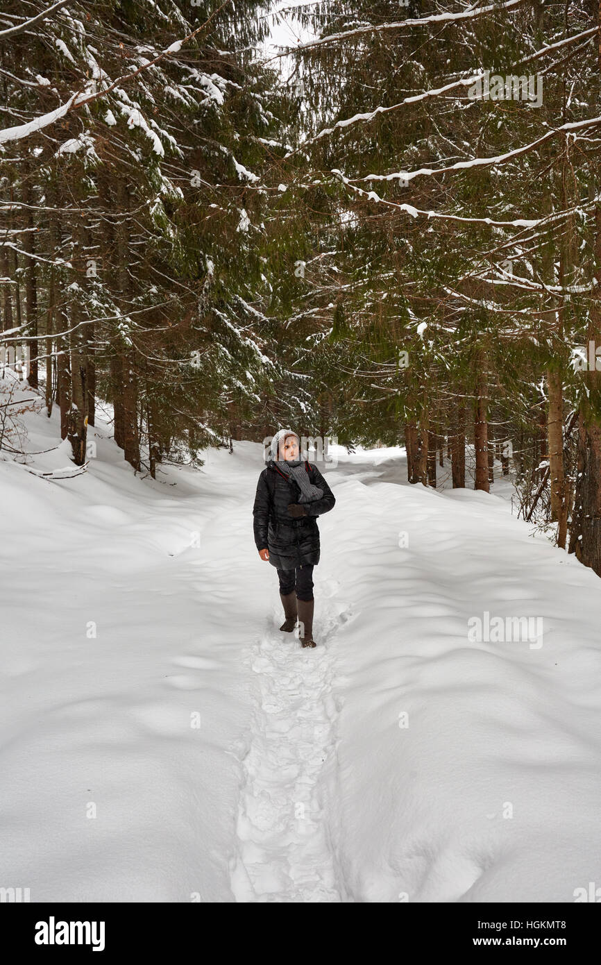 Tourist woman with camera hiking on a snowy trail in the mountains ...