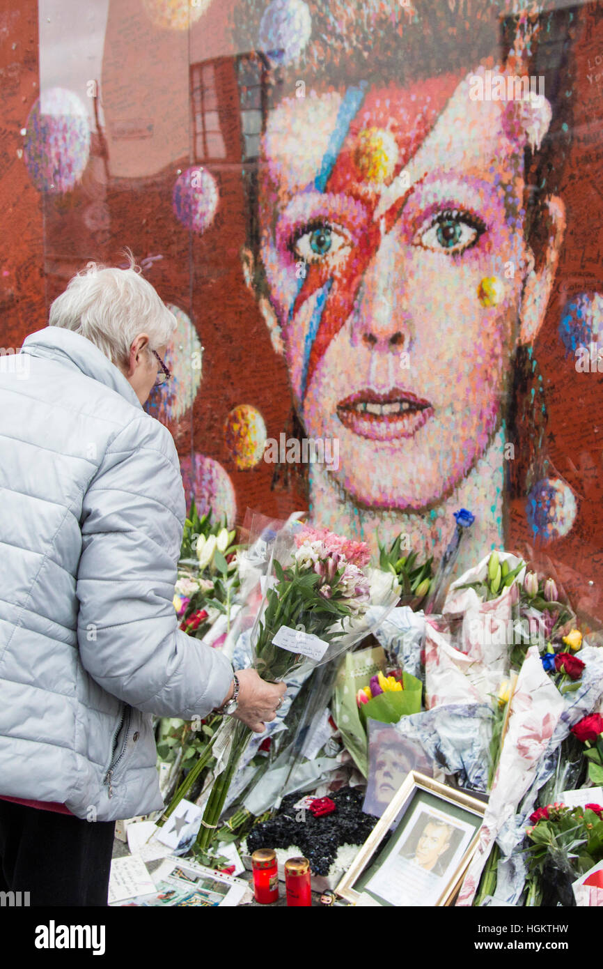 A fan lays flowers at the mural. Fans gather at the David Bowie mural ...