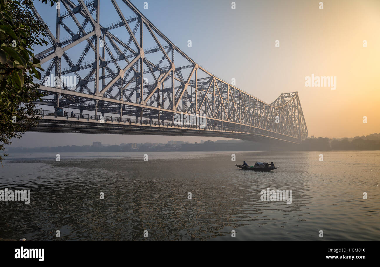 Historic Howrah bridge on  river Ganges on a misty winter morning with a wooden fishing boat passing the bridge. Stock Photo