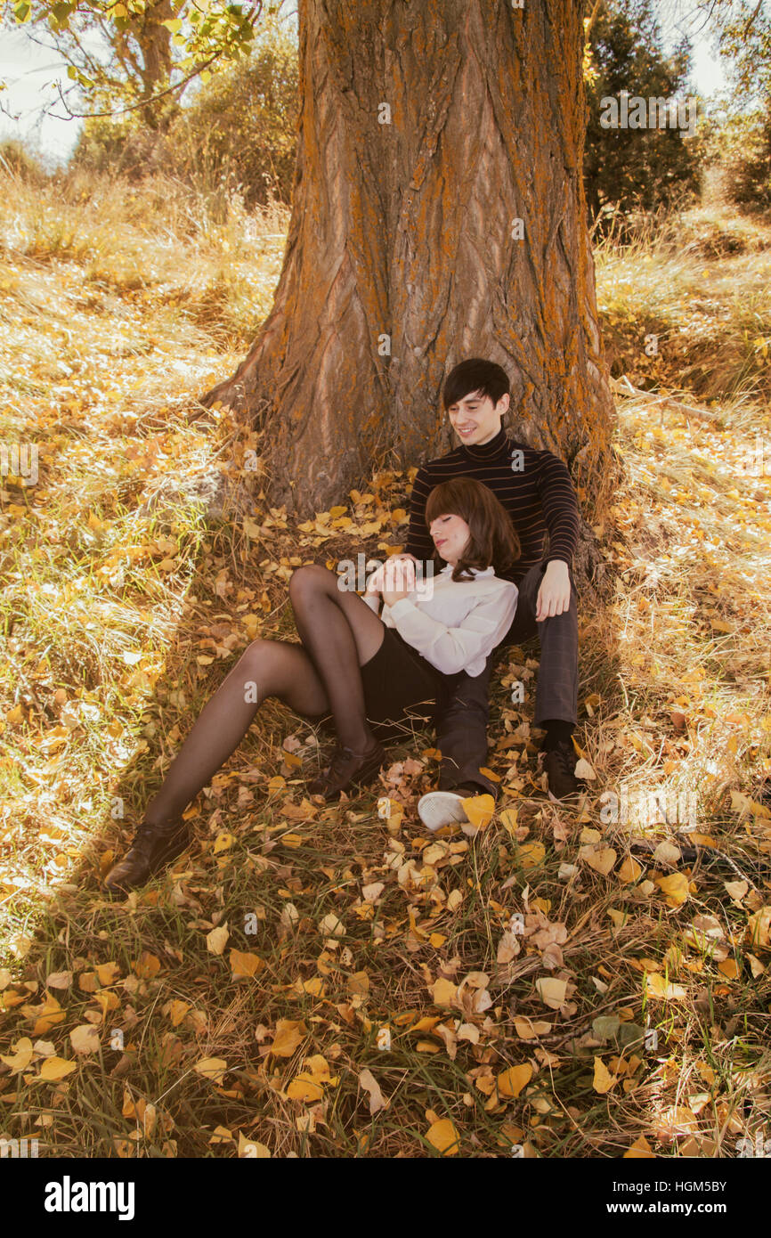 Young couple in a park at autumn, leaning on a tree Stock Photo