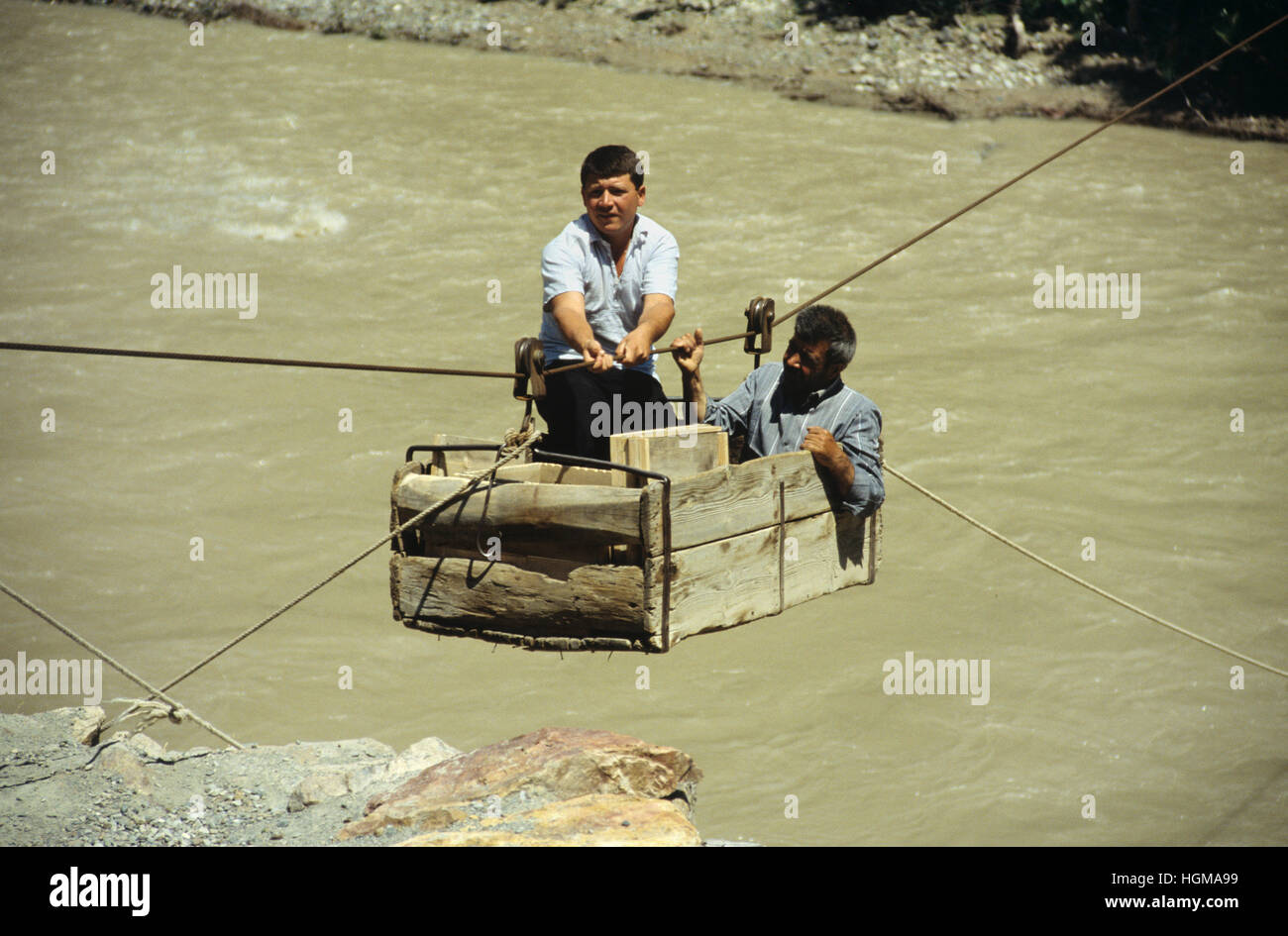 Two Turkih Men in a Zip-line Trolley, aka Zip-wire, Rope or Cable Trolley (and in Turkish as 'Halat'), Crossing the Oltu River, a Tributary of the Coruh River, in north-east Turkey Stock Photo