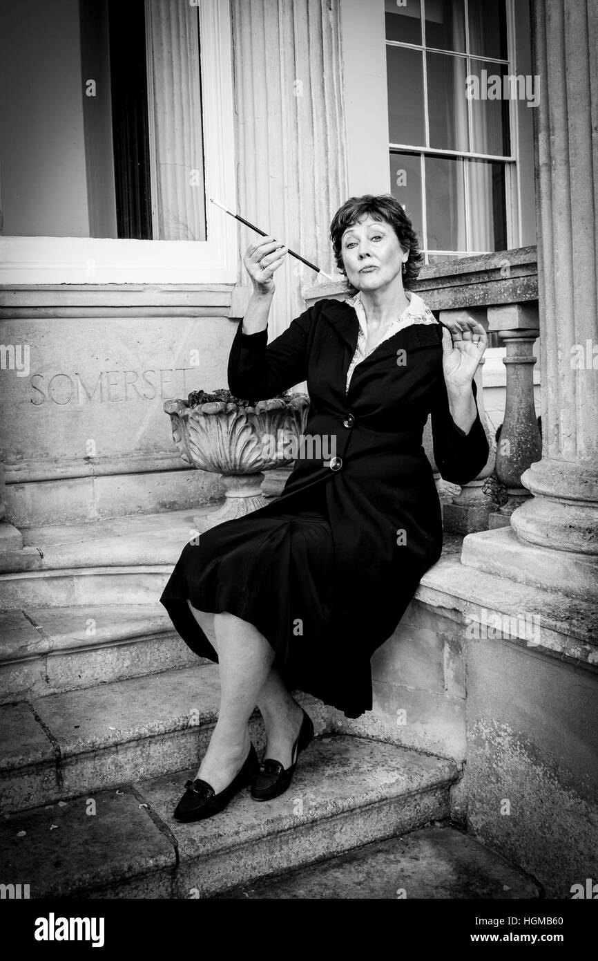 English Edwardian aristocratic lady sat on steps of stately home with cigarette and cigarette holder Stock Photo