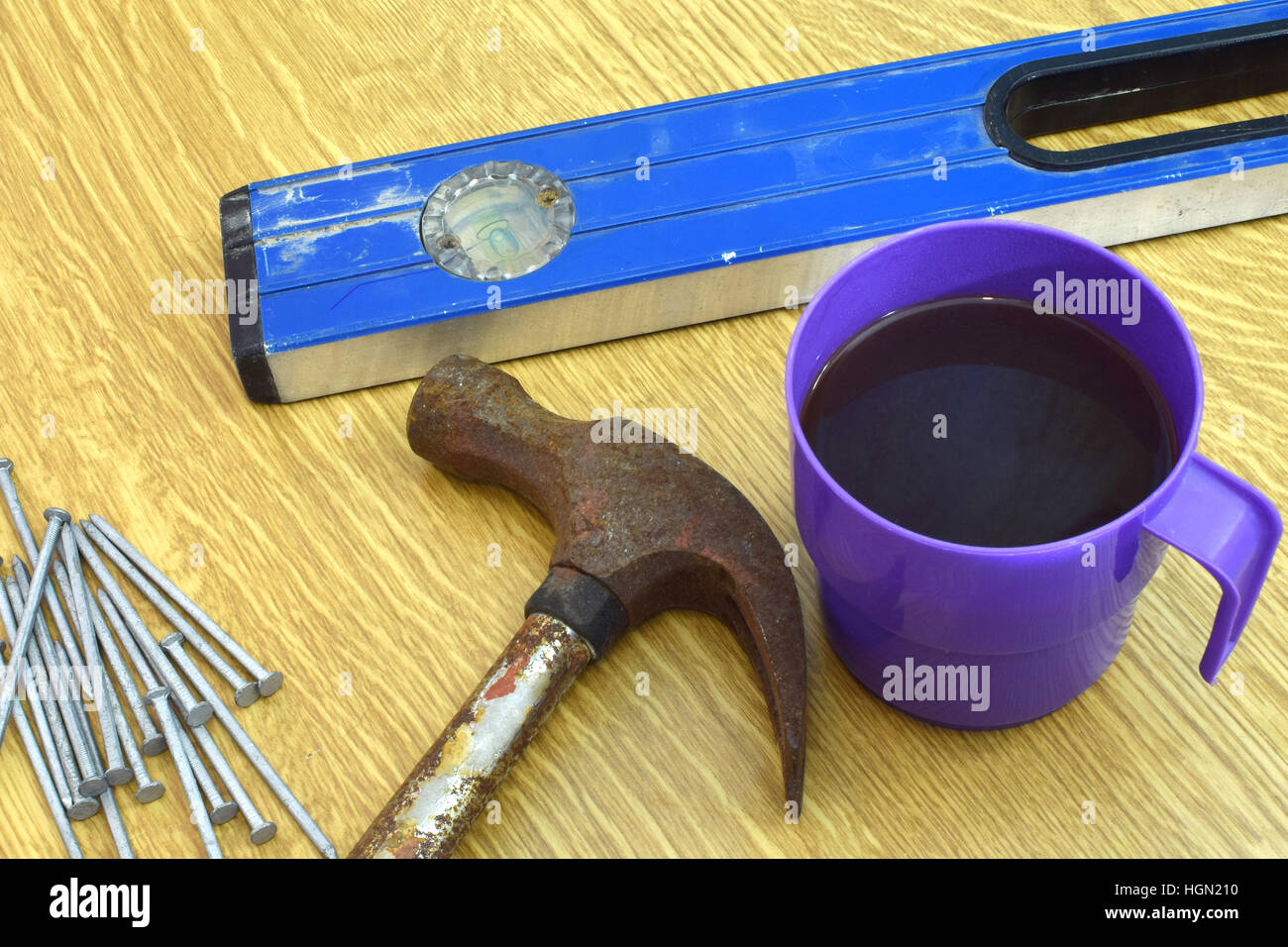 Coffee mug, old hammer, nails and spirit level on the table. Stock Photo
