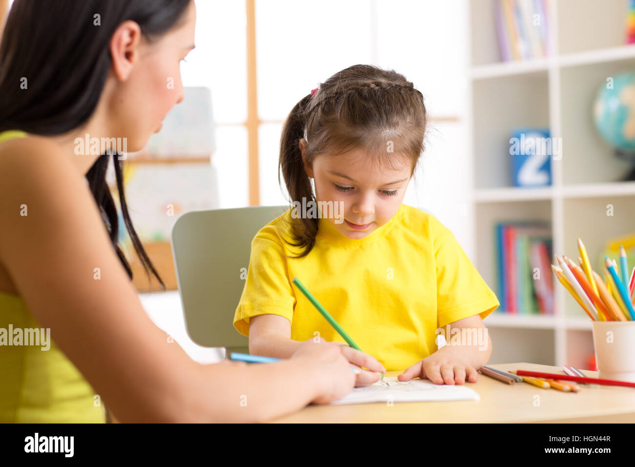 Woman teaching kid to write. Elementary pupil painting with teacher Stock Photo